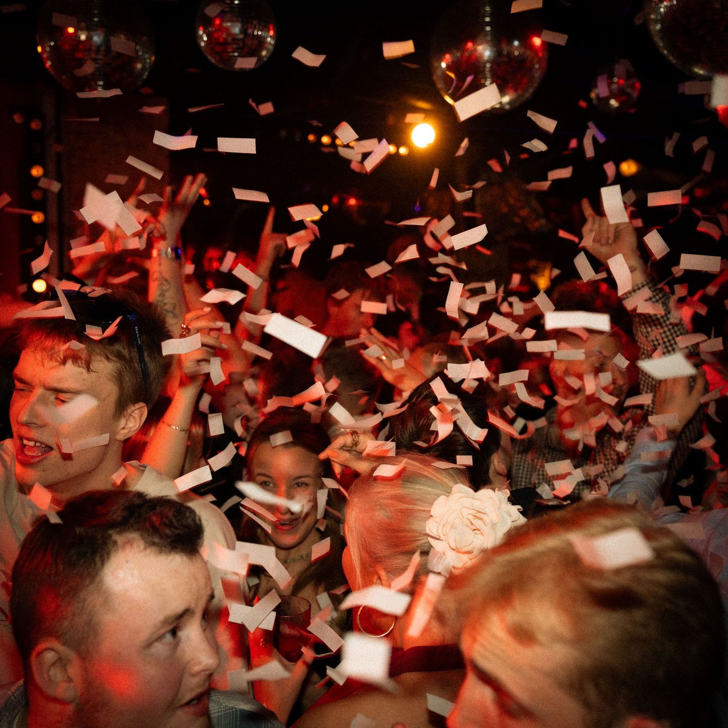 Confetti explosion over a crowd in a nightclub bathed in red lighting.