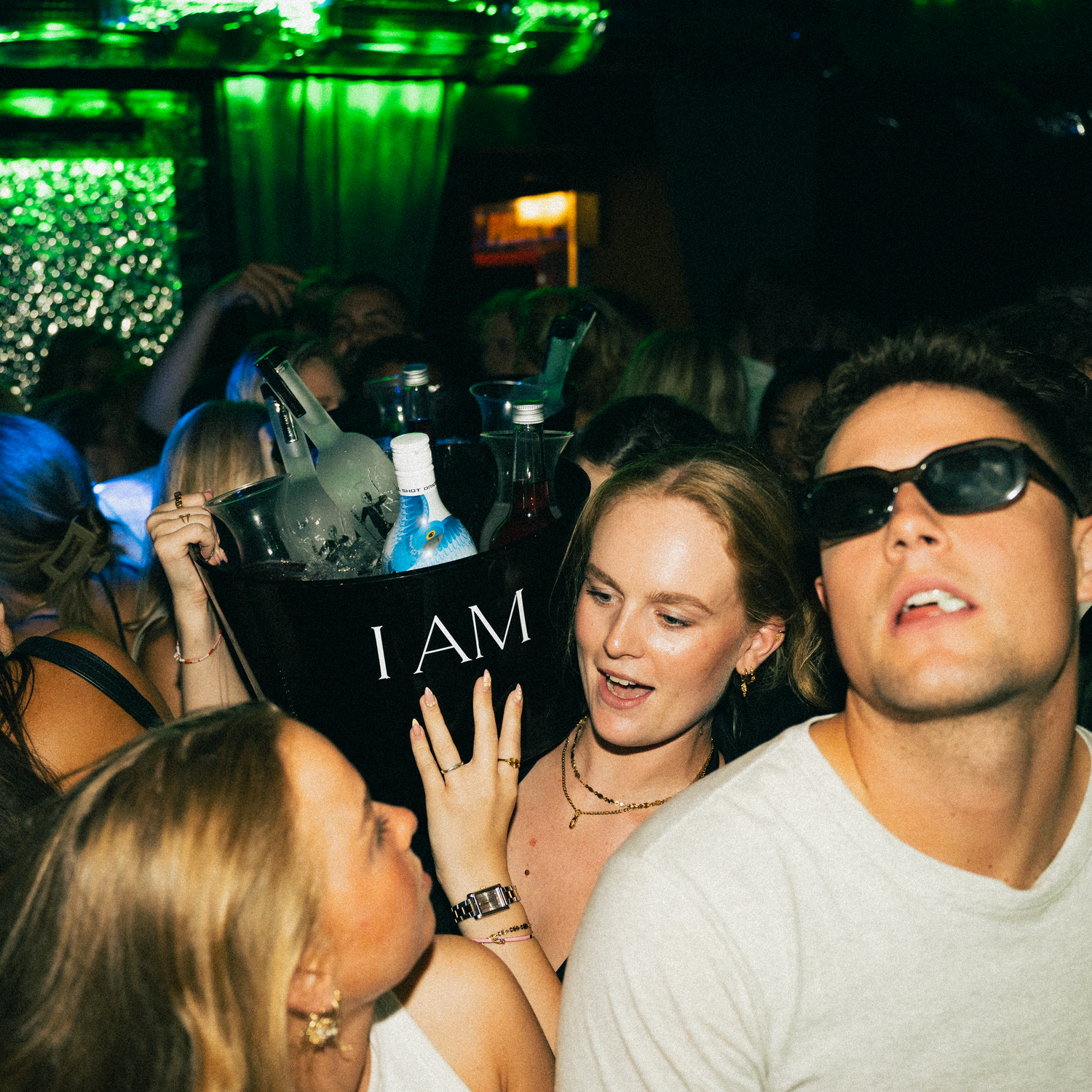 People partying at a nightclub with green lighting and a dark atmosphere.