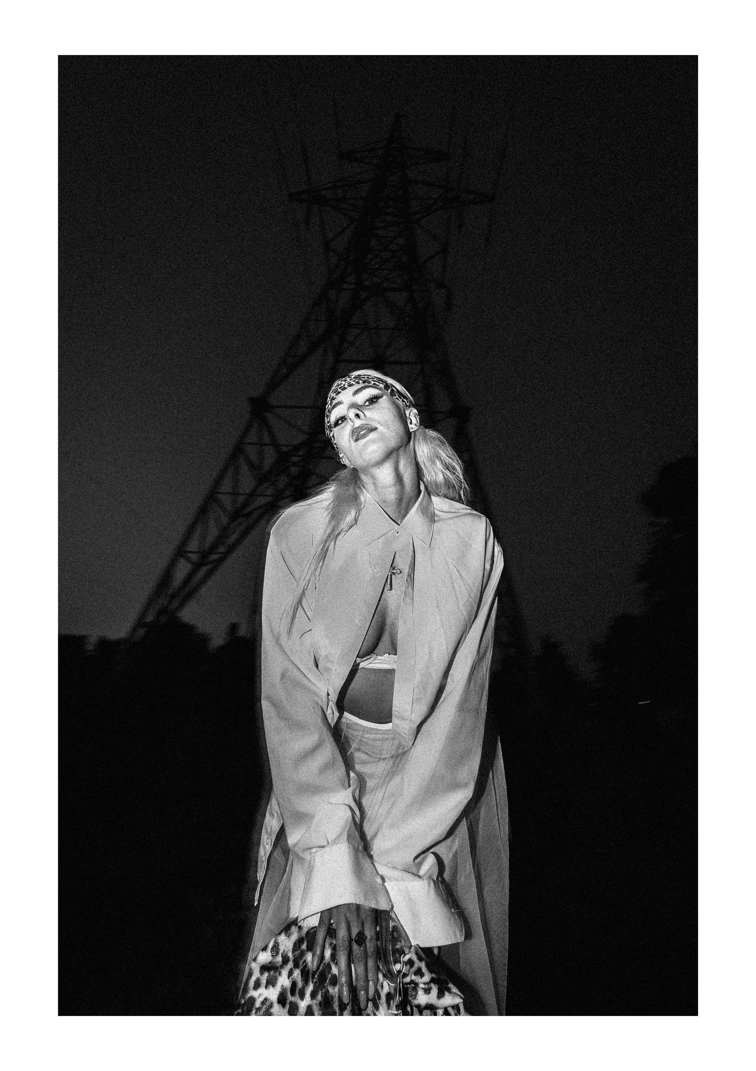 Black and white fashion photo with power lines silhouetted against dark sky, featuring stylish oversized jacket and skirt.