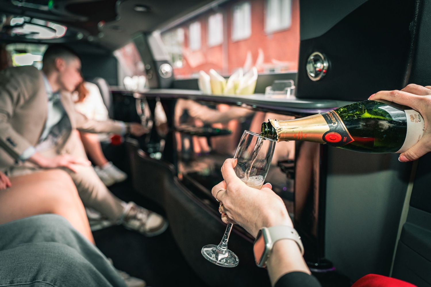Someone pouring champagne into a glass in a dimly lit restaurant setting with people seated in the background.