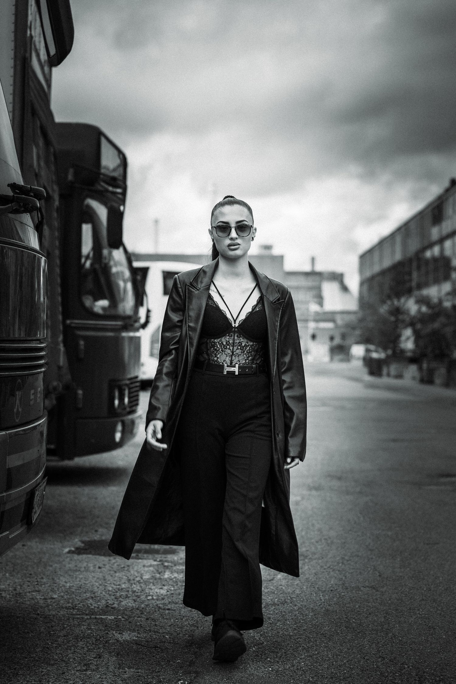 Black and white series shows a young figure walking along a gritty urban street in a stylish dark outfit.