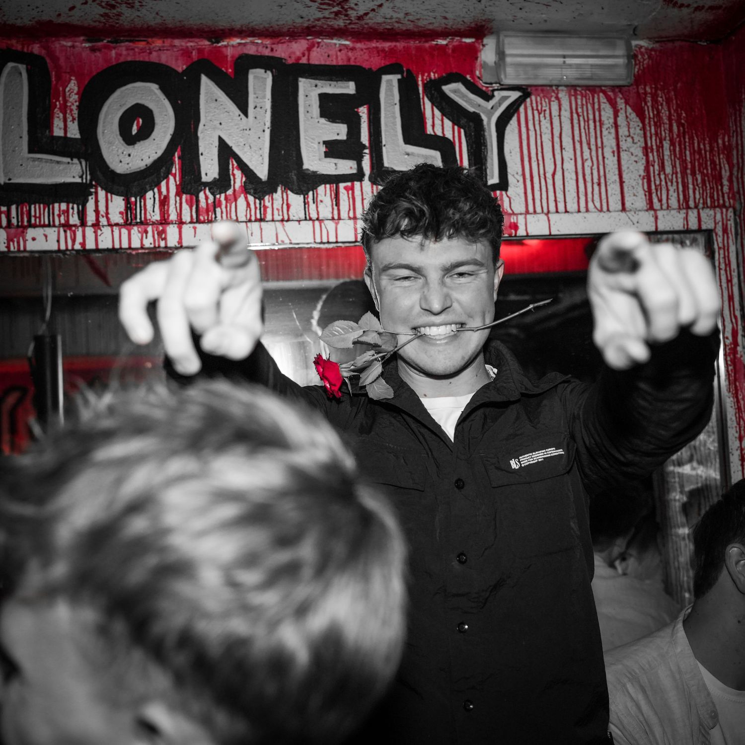 Black and white photo with red text reading LONELY on wall while person pointing enthusiastically at camera.