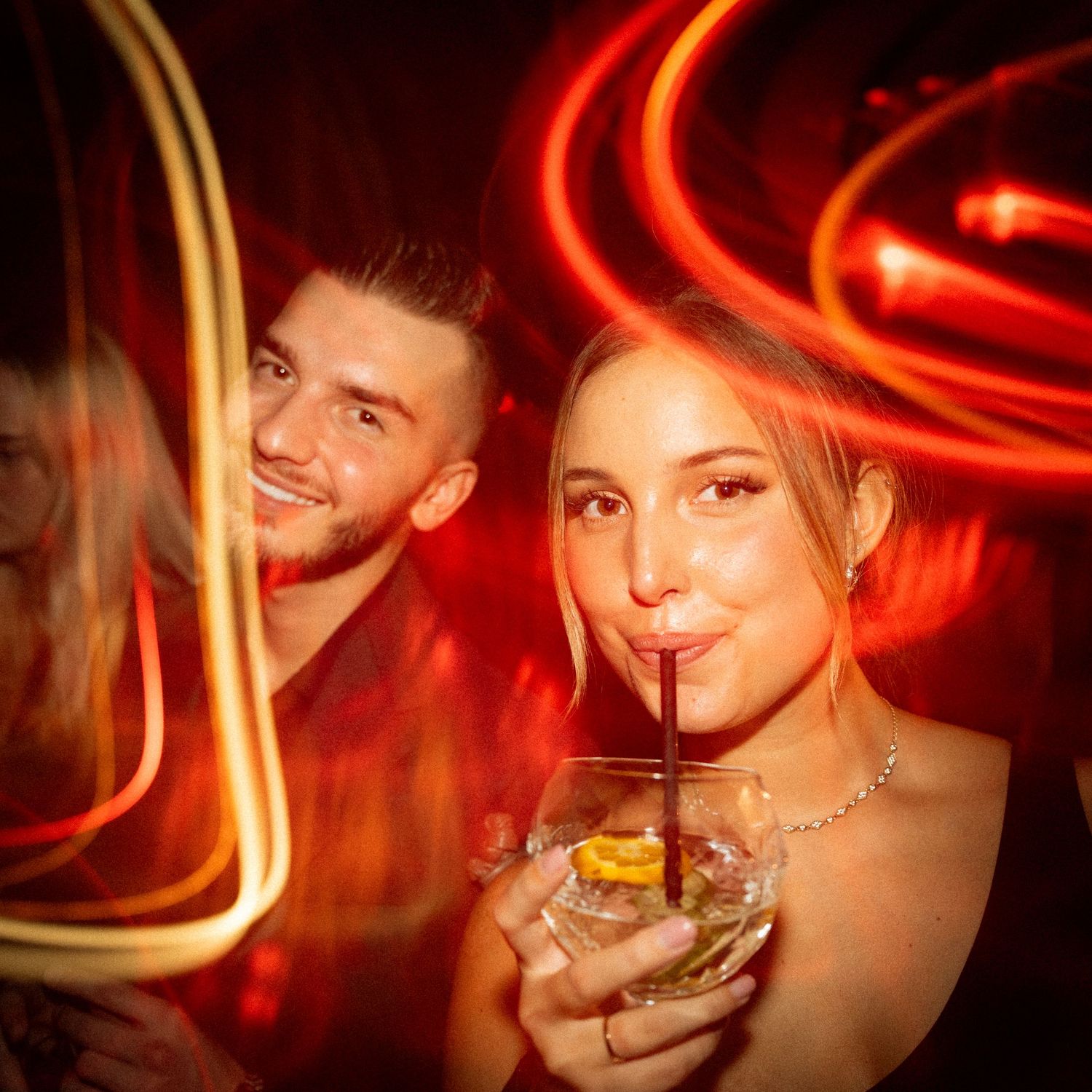 Nightclub scene with red neon lighting and cocktail glass in foreground.