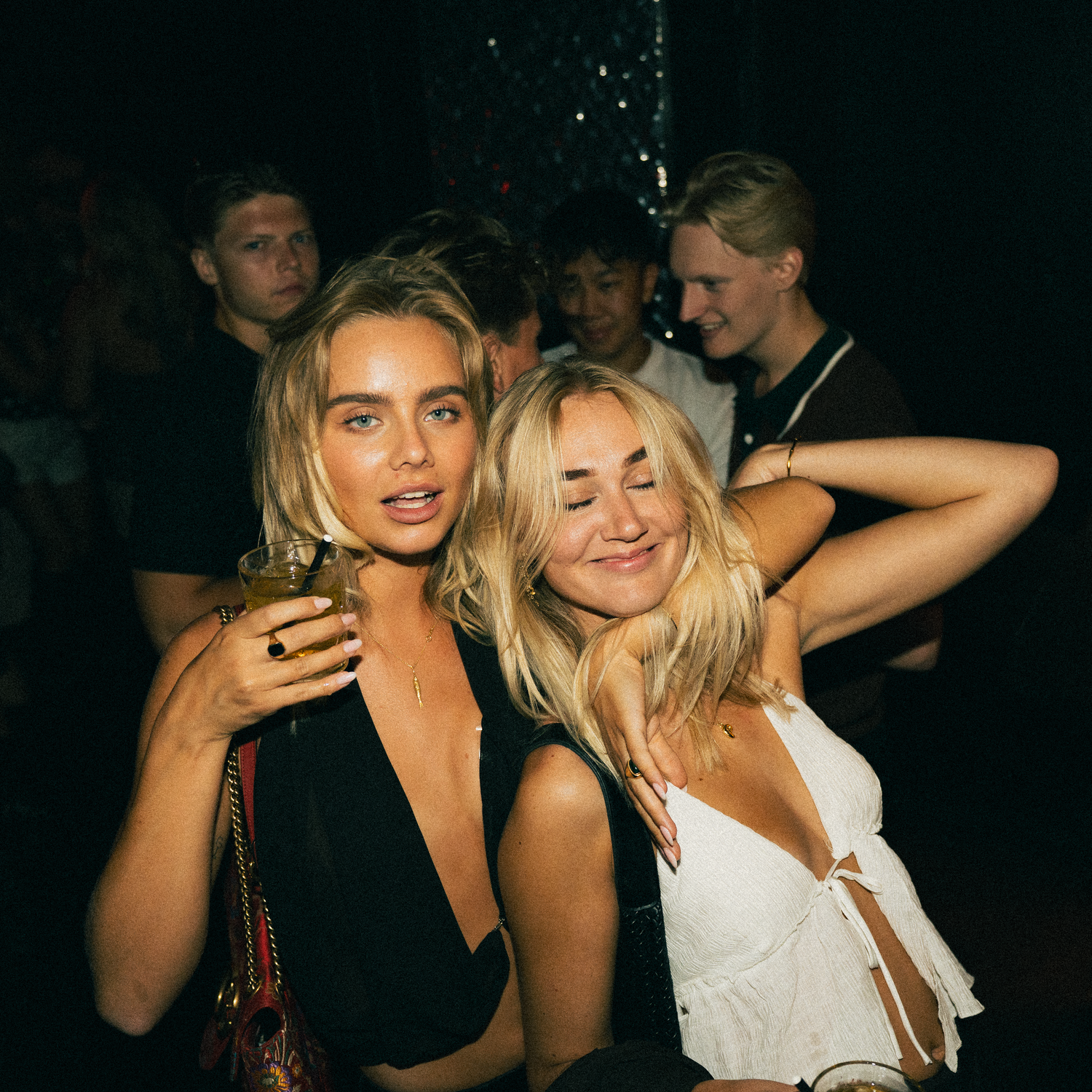 Group of friends enjoying a night out at a dimly lit party venue, laughing and socializing together.