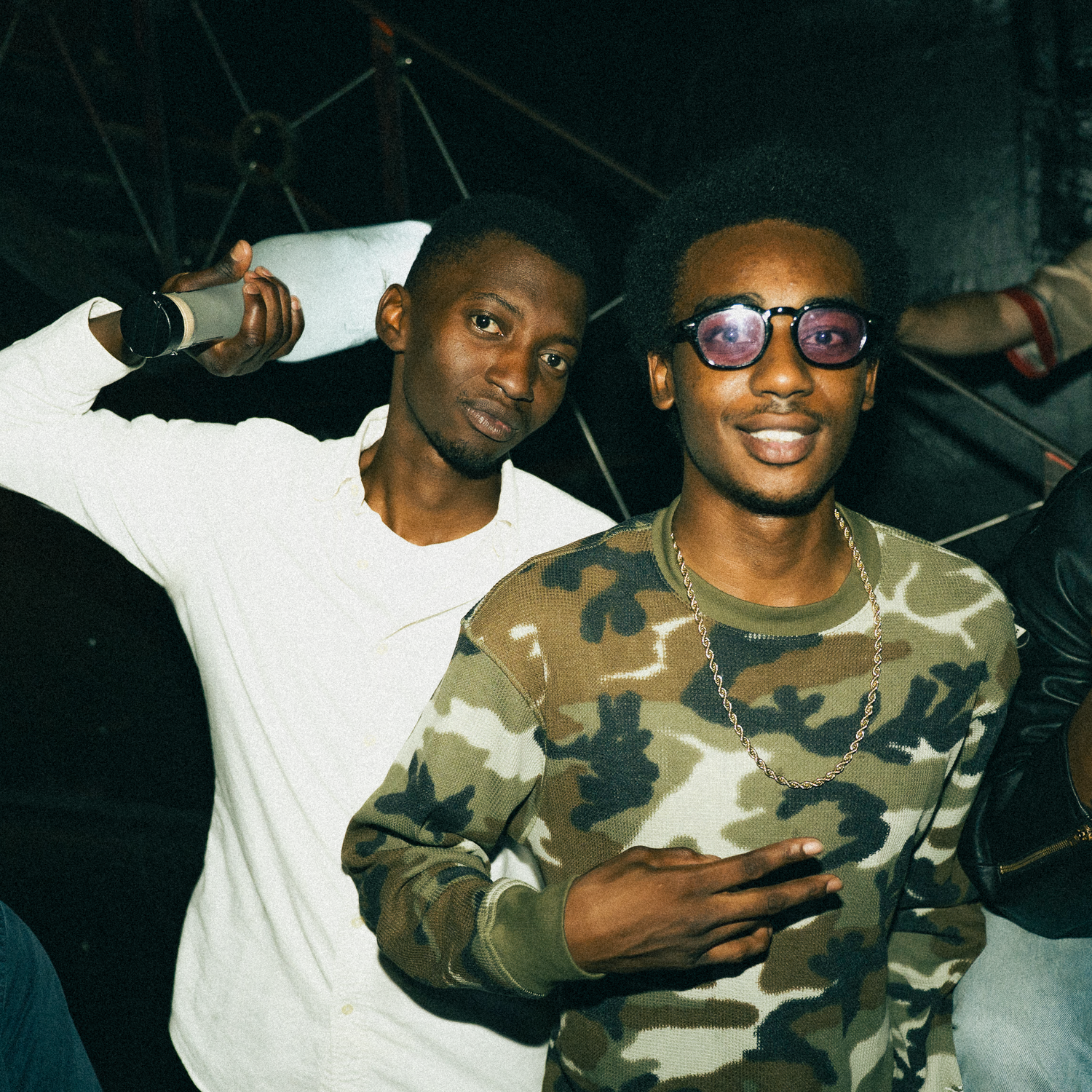 Person wearing camo print jacket and glasses posing in series of dark-lit photos.