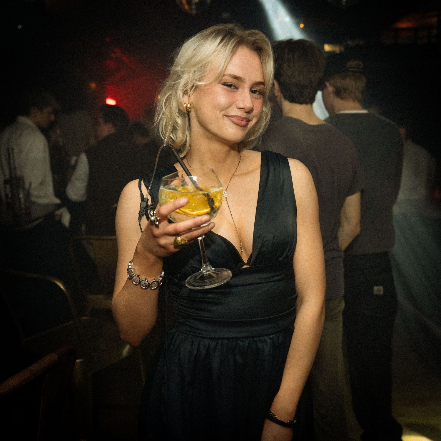 Person i sort kjole holder en drink på natklub med dæmpet lys.