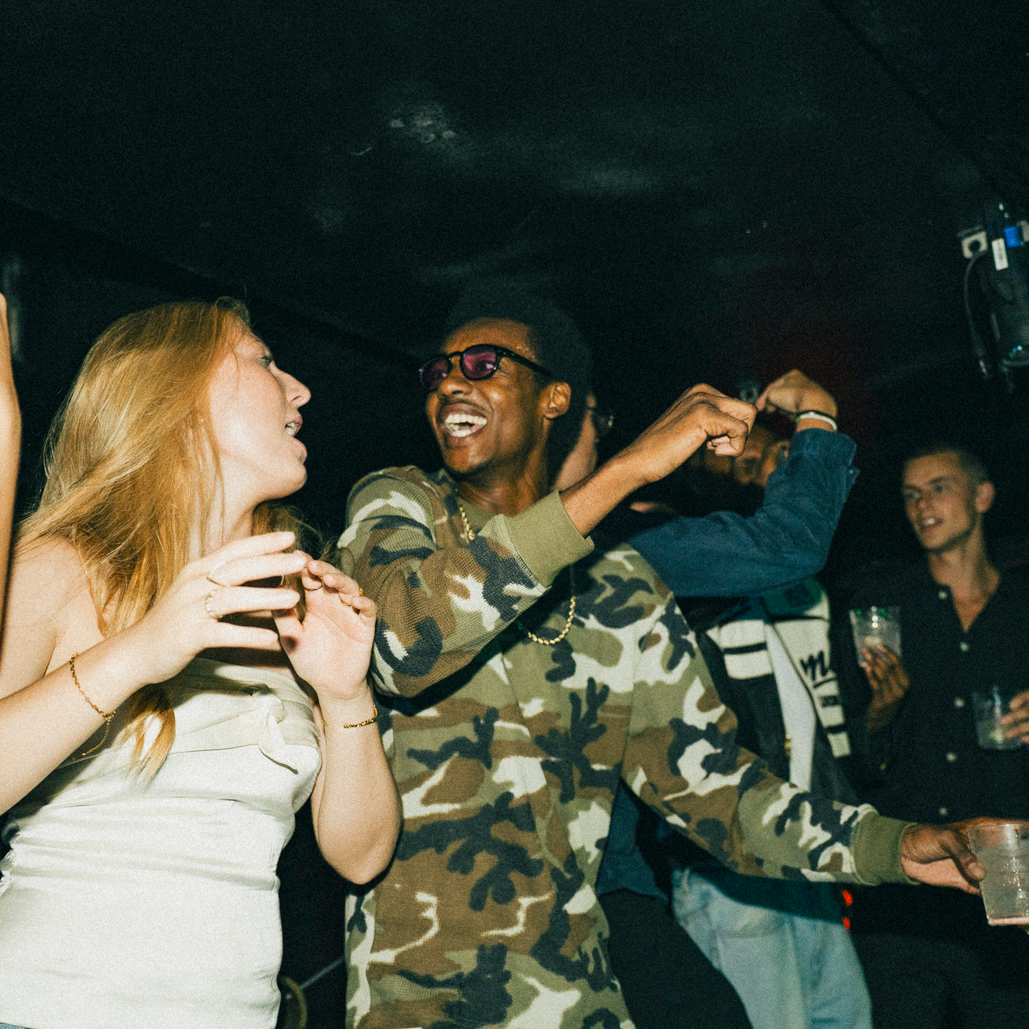 A group of people enjoying a lively night out at a dark club or party venue with animated expressions and gestures.