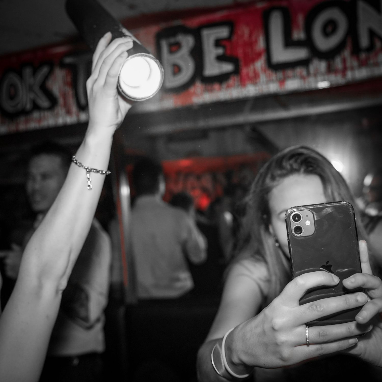 Person holding phone and another holding flashlight in dark nightclub with neon signs in background.
