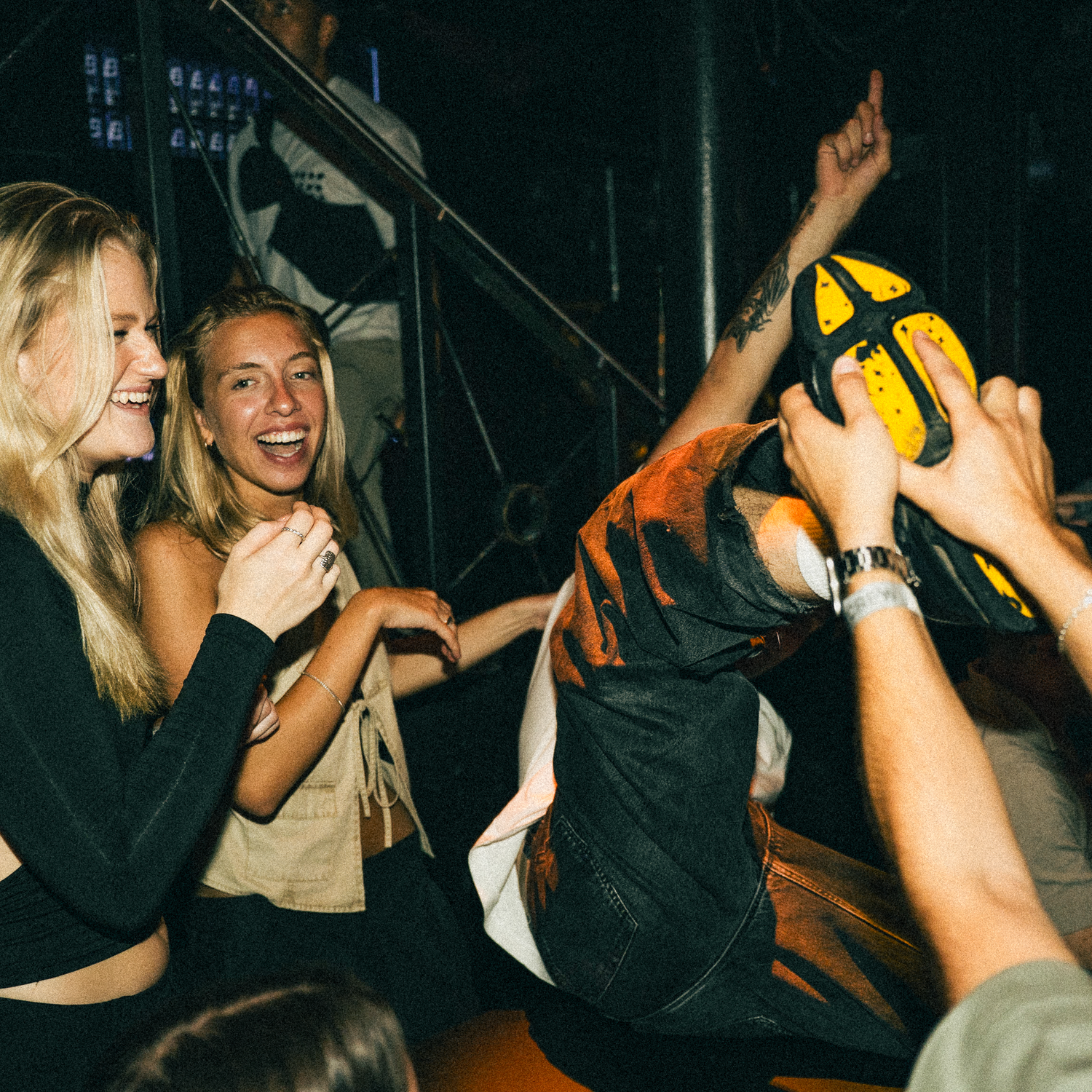People dancing and celebrating at a nightclub with their arms raised in the dark club atmosphere.