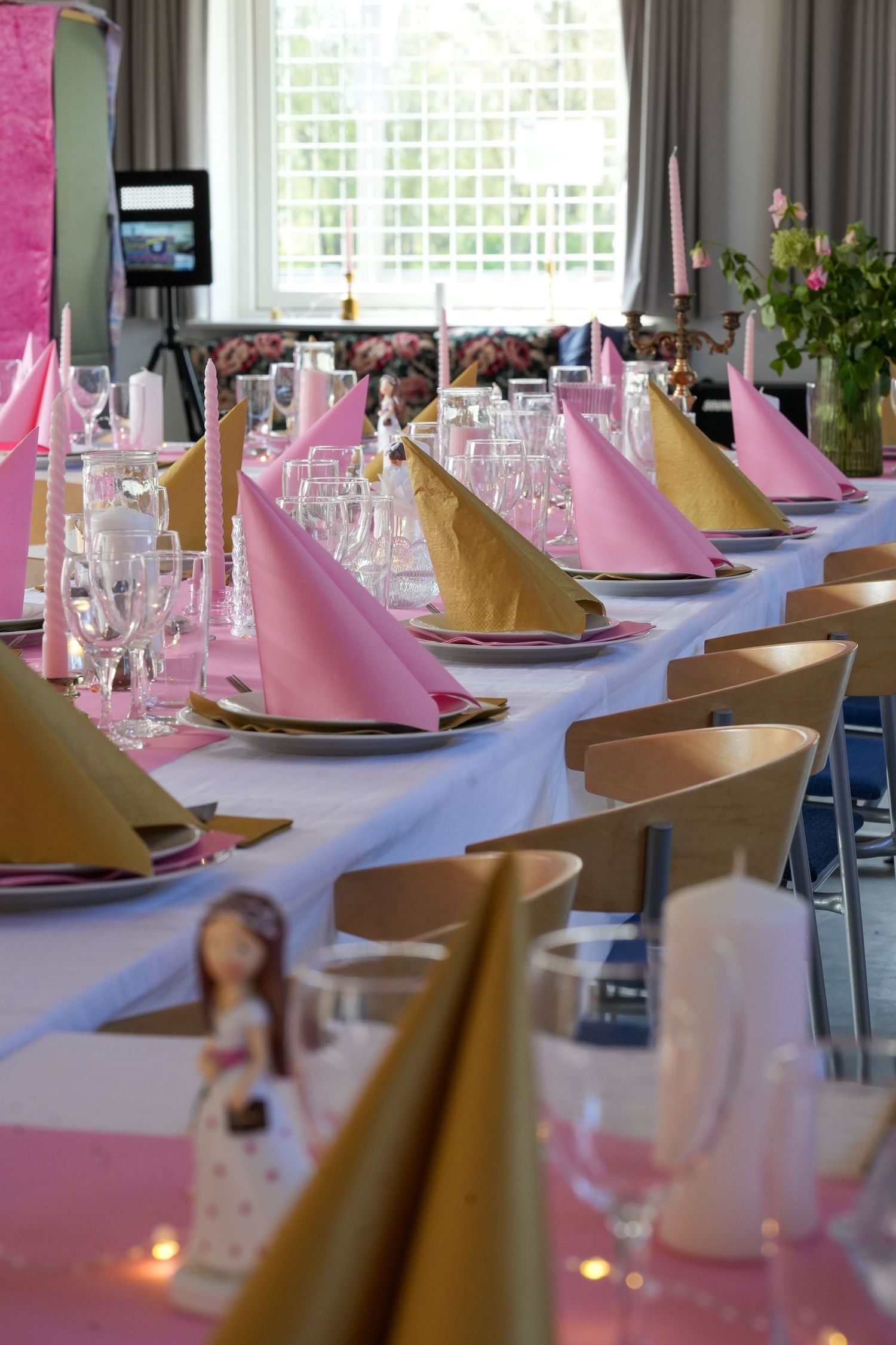 Elegant table setting with pink and gold napkins arranged on a long white tablecloth for a formal celebration or event.