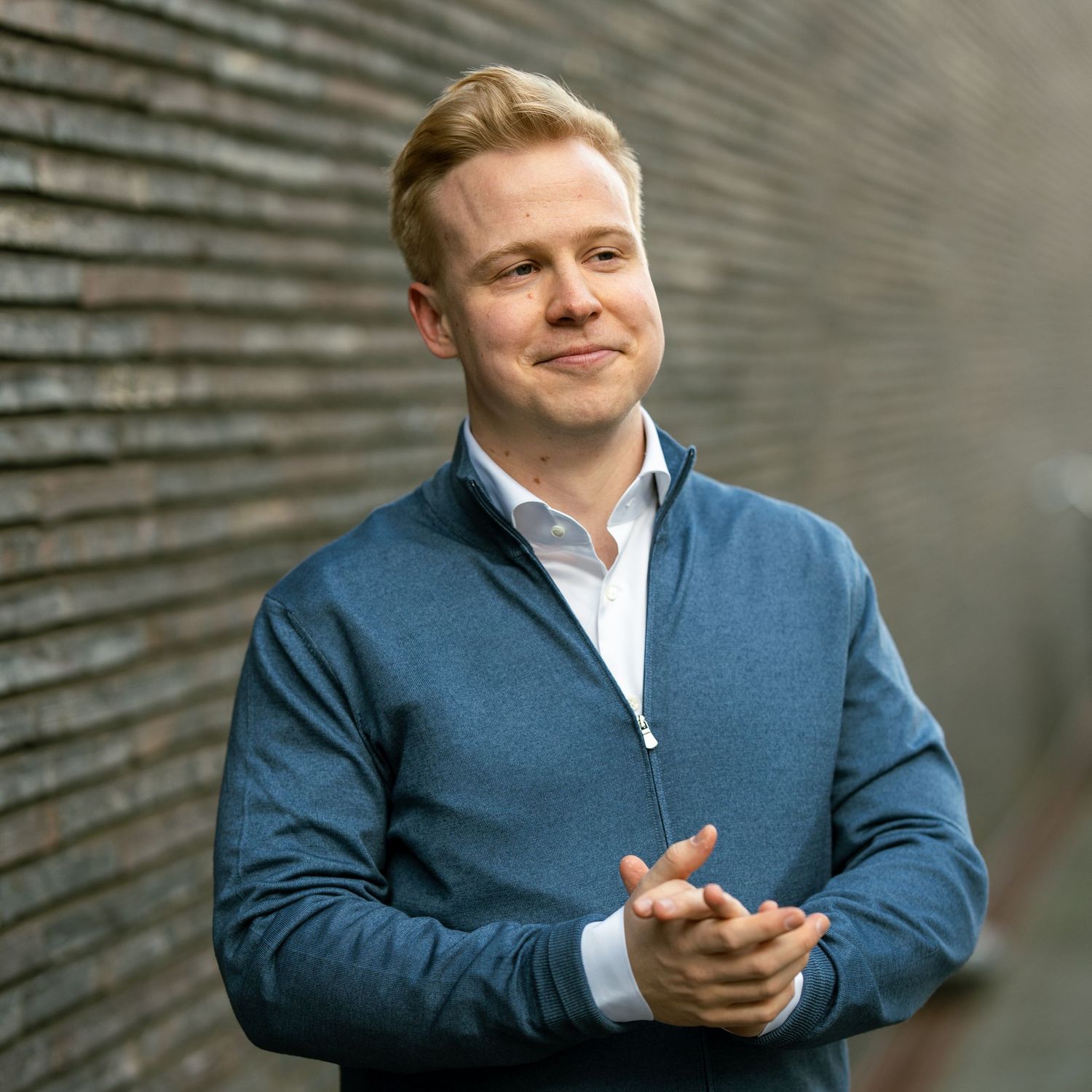 Professional in a blue quarter-zip sweater and white shirt clasps hands while smiling.