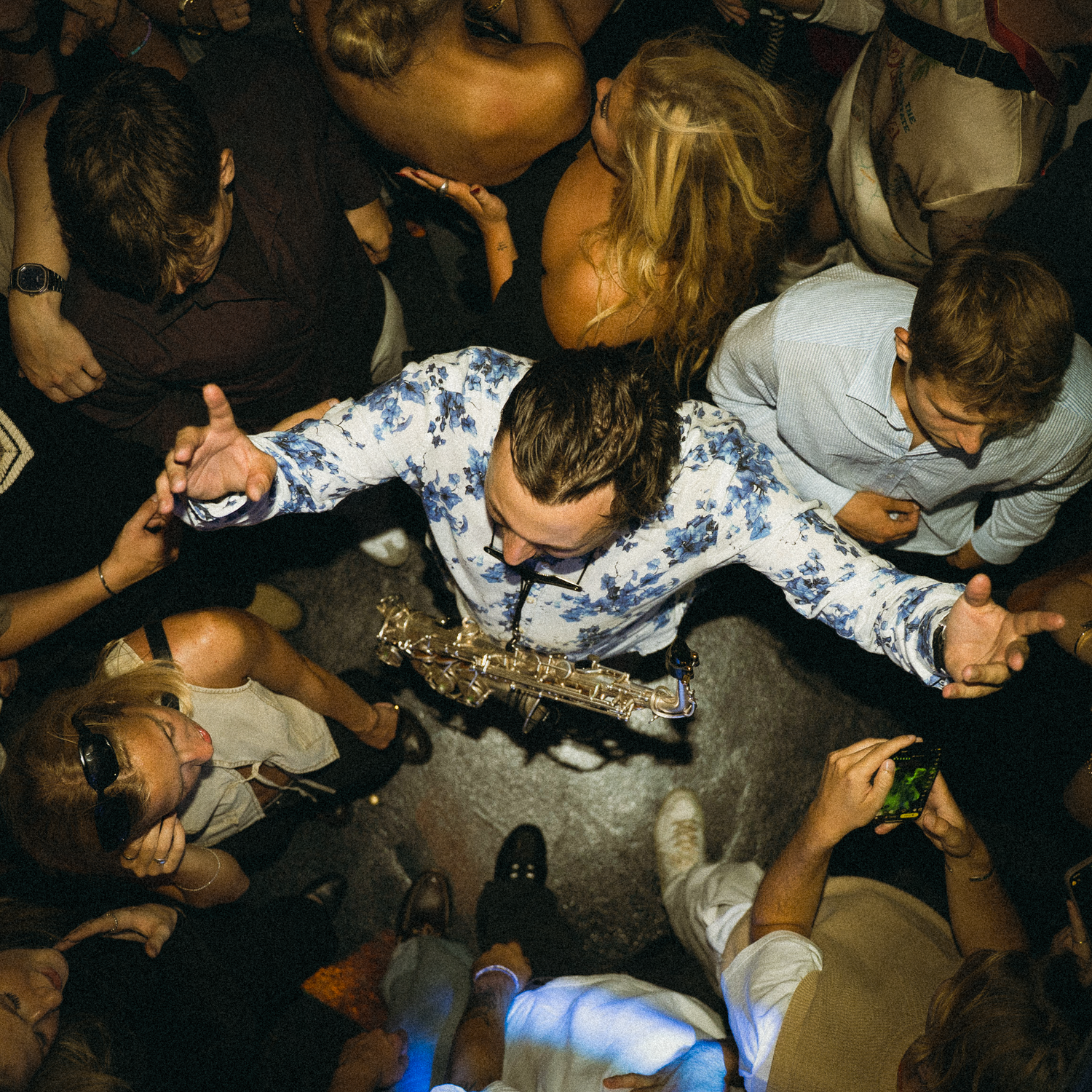 Overhead view of people huddled in a dark room gathered around a bright spot in a crowded club setting.