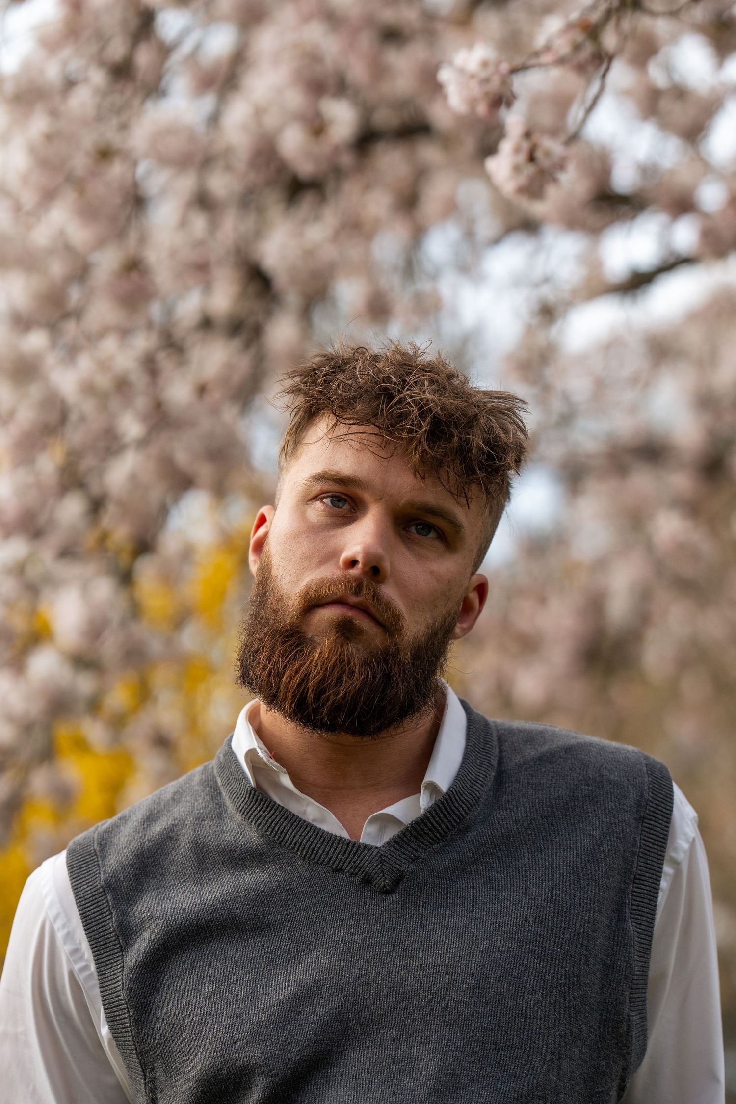 Portrait in vest and white shirt against blossoming cherry trees.