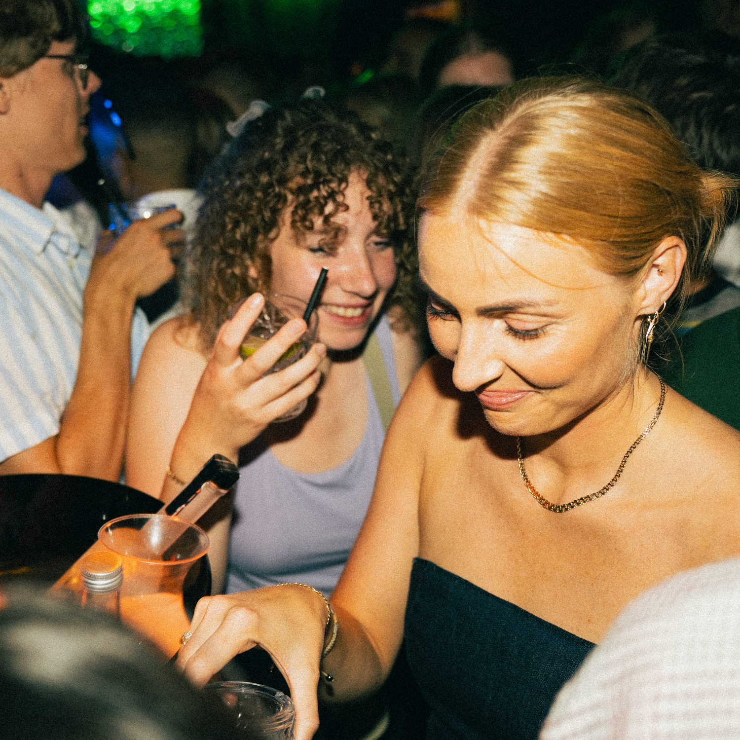 Two friends laughing and enjoying themselves at a nightclub with colorful lighting in the background.