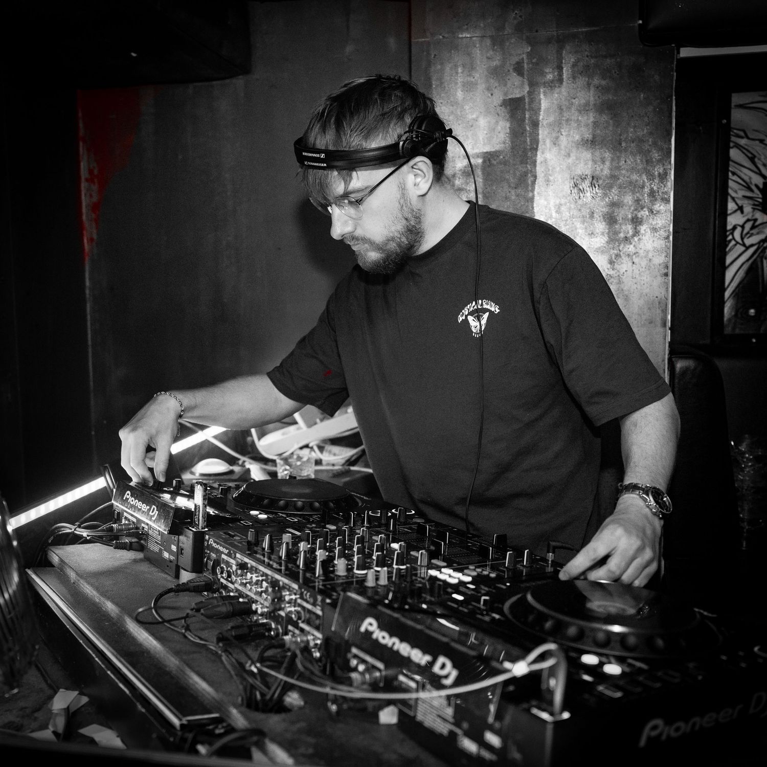 En DJ optræder på professionelt udstyr i en mørk natklub, fanget i sort-hvid.