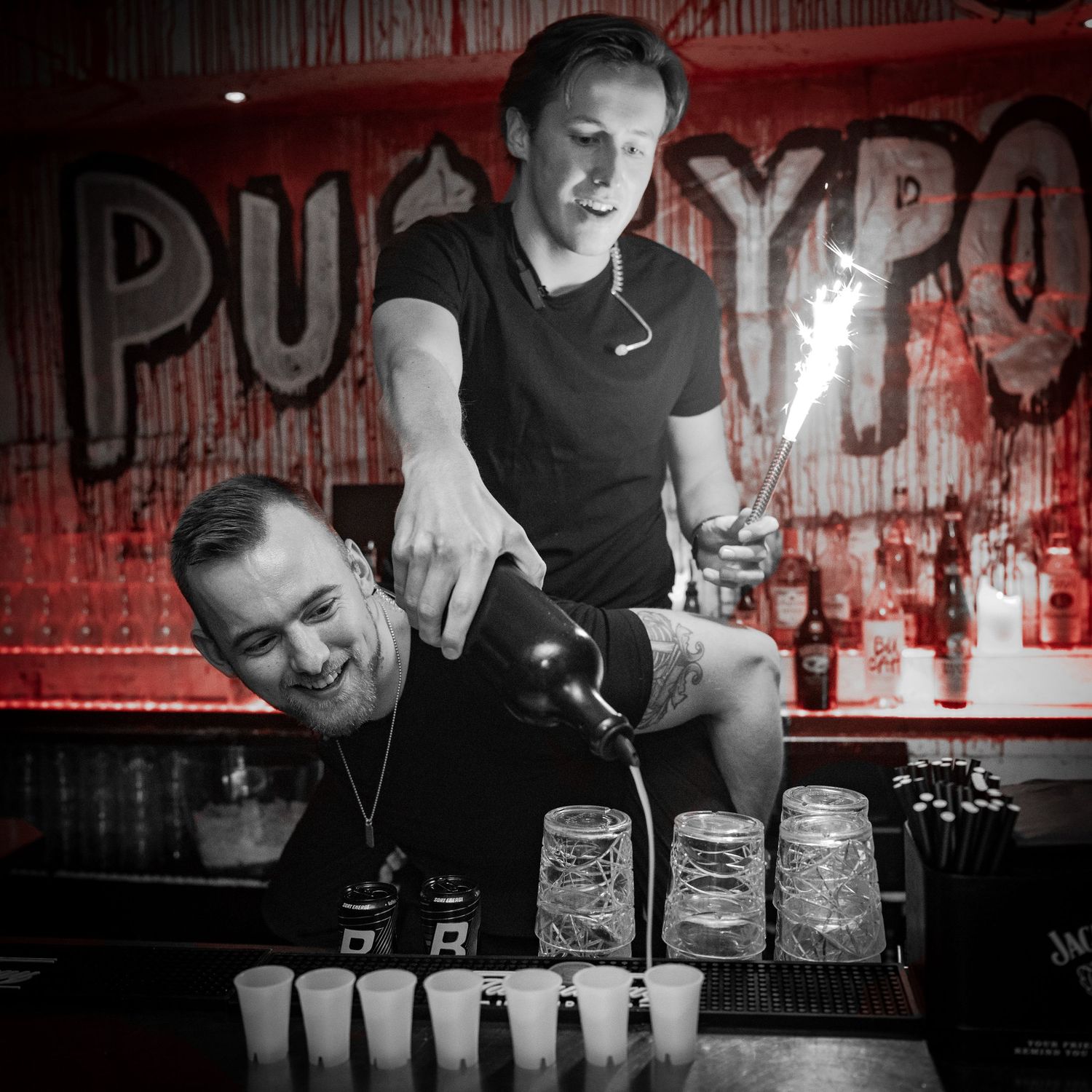 Bartenders pouring drinks at a bar with red lighting.