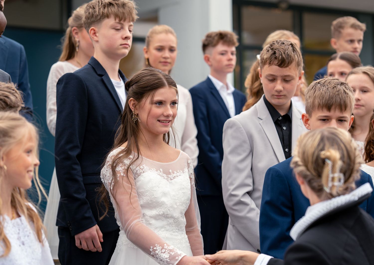 A group of students in formal attire including navy suits and white dress gather together at what appears to be a ceremony.