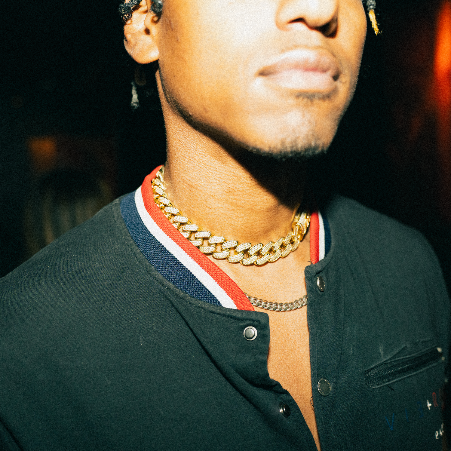 Person wearing a black top and gold chain necklace smiling in a dark setting.