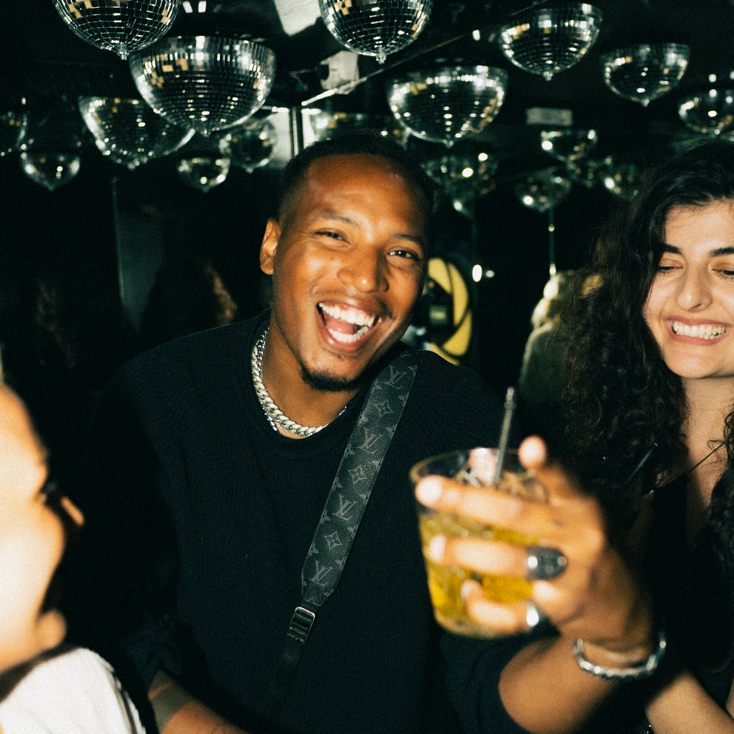 People enjoying themselves at a nightclub with disco balls overhead and drinks in hand at a lively party.