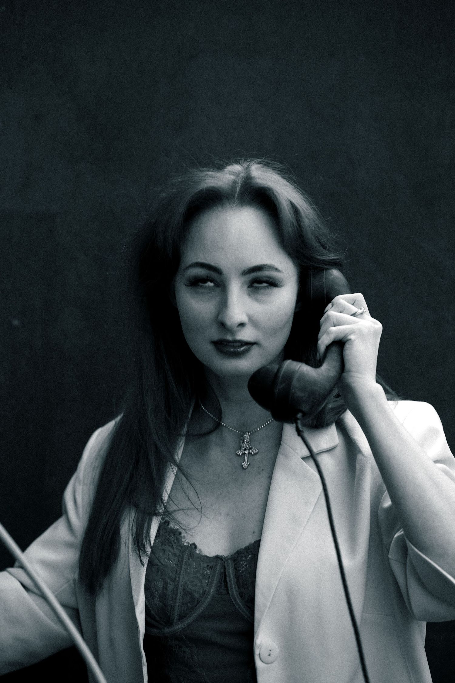 A vintage-style black and white portrait showing someone holding an old telephone receiver against a dark background.
