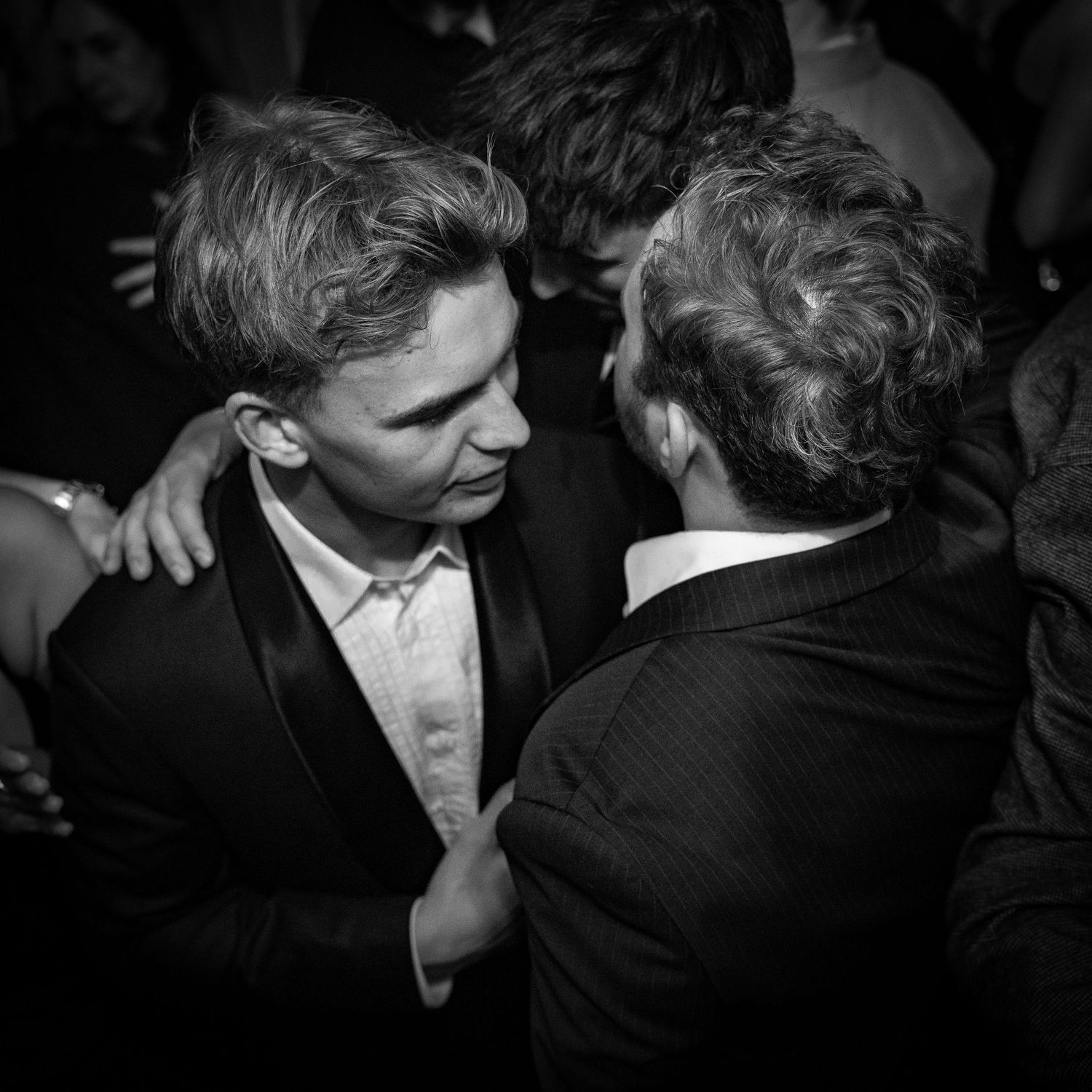 To personer deler et intimt øjeblik i formelt tøj til en svagt oplyst fest eller natklub.