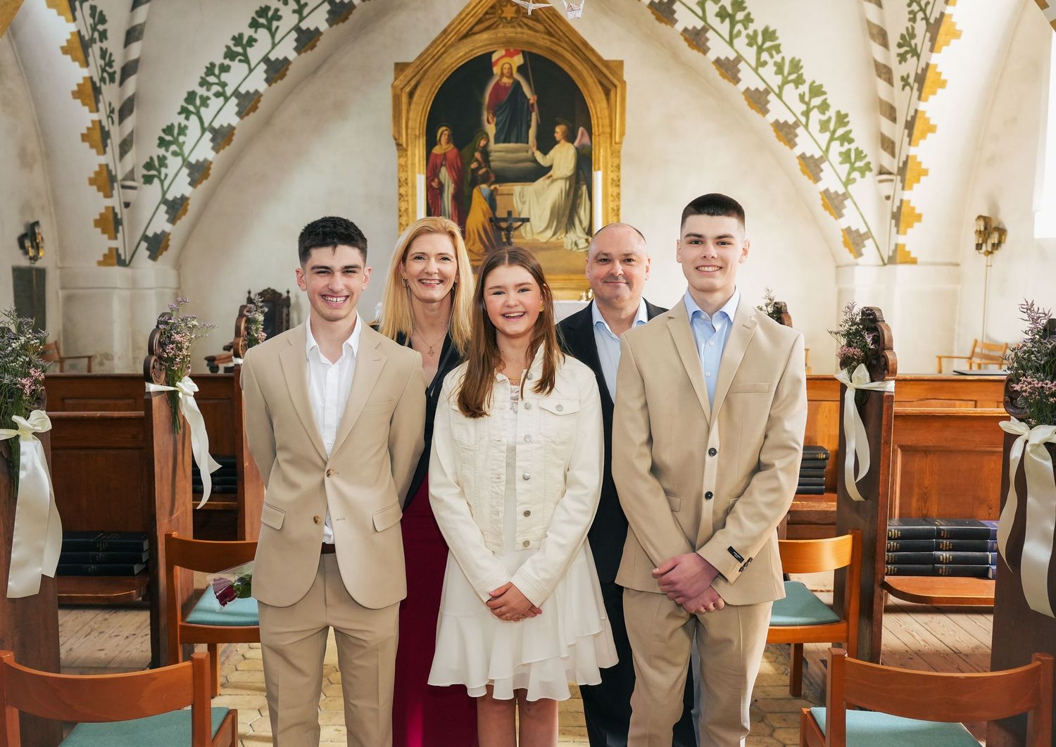 A group stands together in a church sanctuary with ornate painted arches and religious artwork in the background.