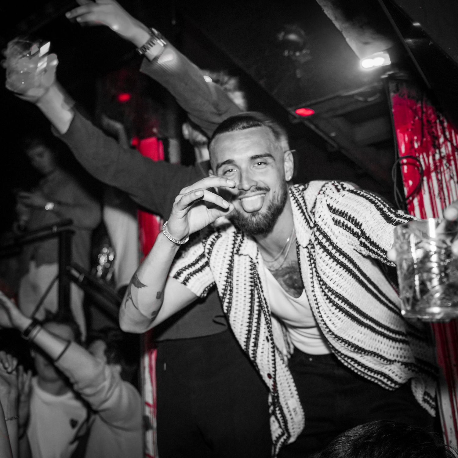 Black and white photo of a smiling person in a striped shirt dancing at a nightclub with party lighting in the background.