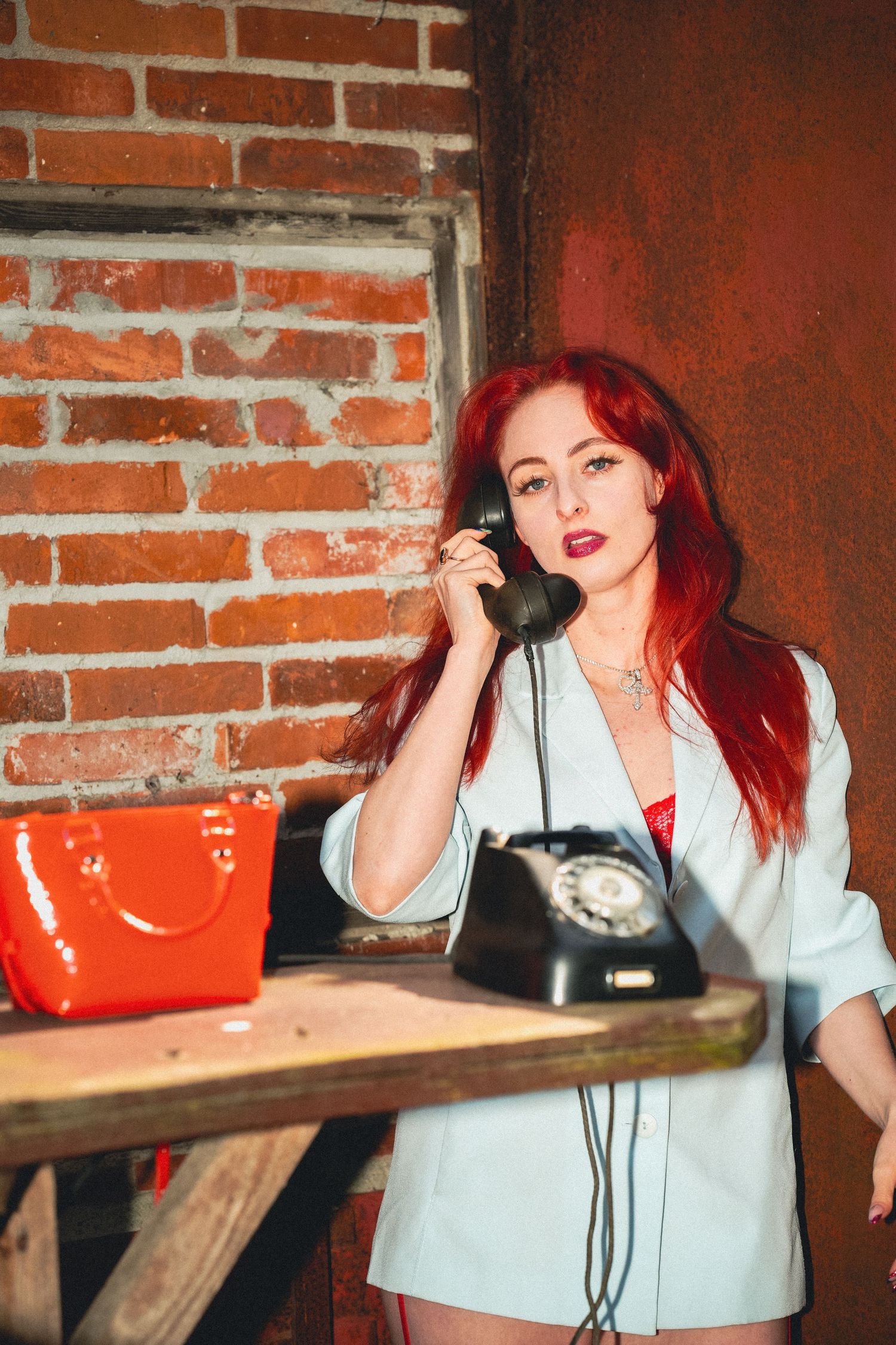 Vintage scene with rotary telephone on wooden table next to bright orange purse against brick wall backdrop.