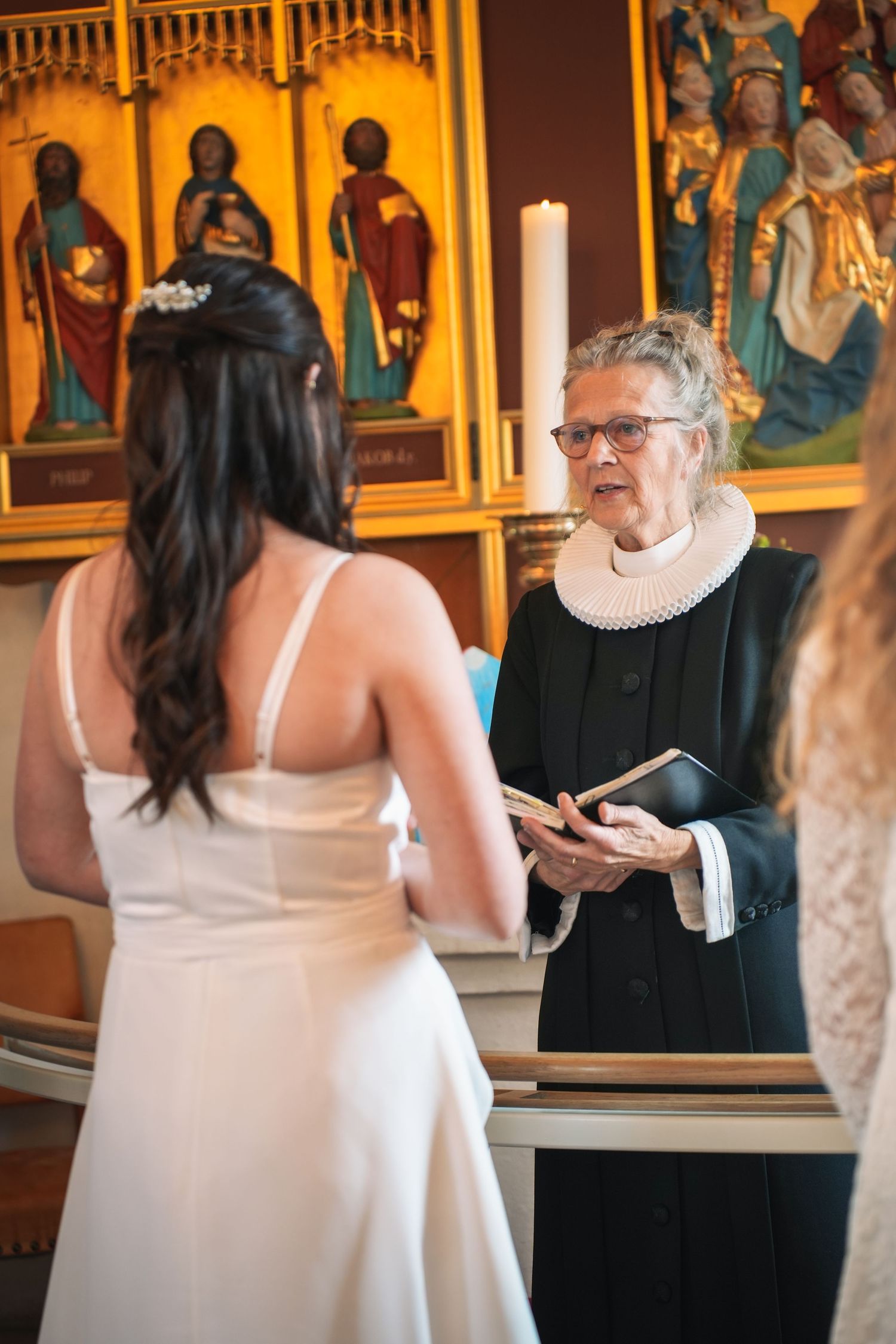 A traditional wedding ceremony takes place inside a church with religious artwork and stained glass in the background.