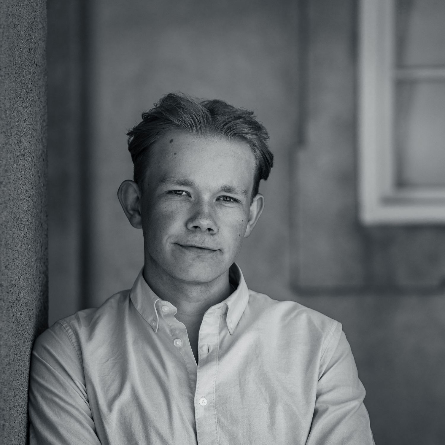 Black and white portrait of a young person in a white button-down shirt looking directly at camera with soft lighting.