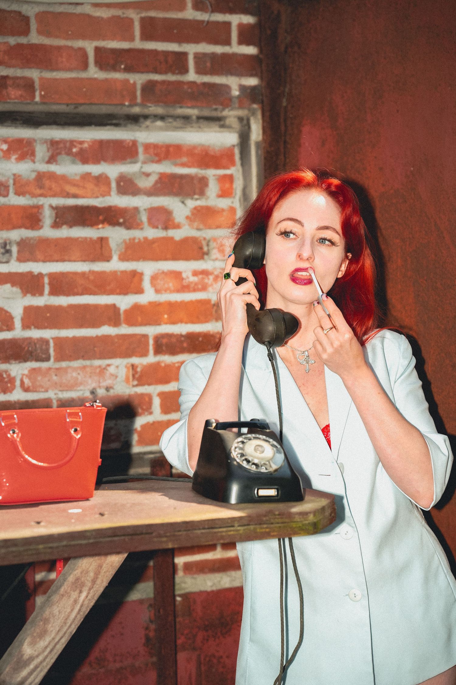 A retro-styled scene with vibrant red hair and vintage rotary phone against exposed brick wall.