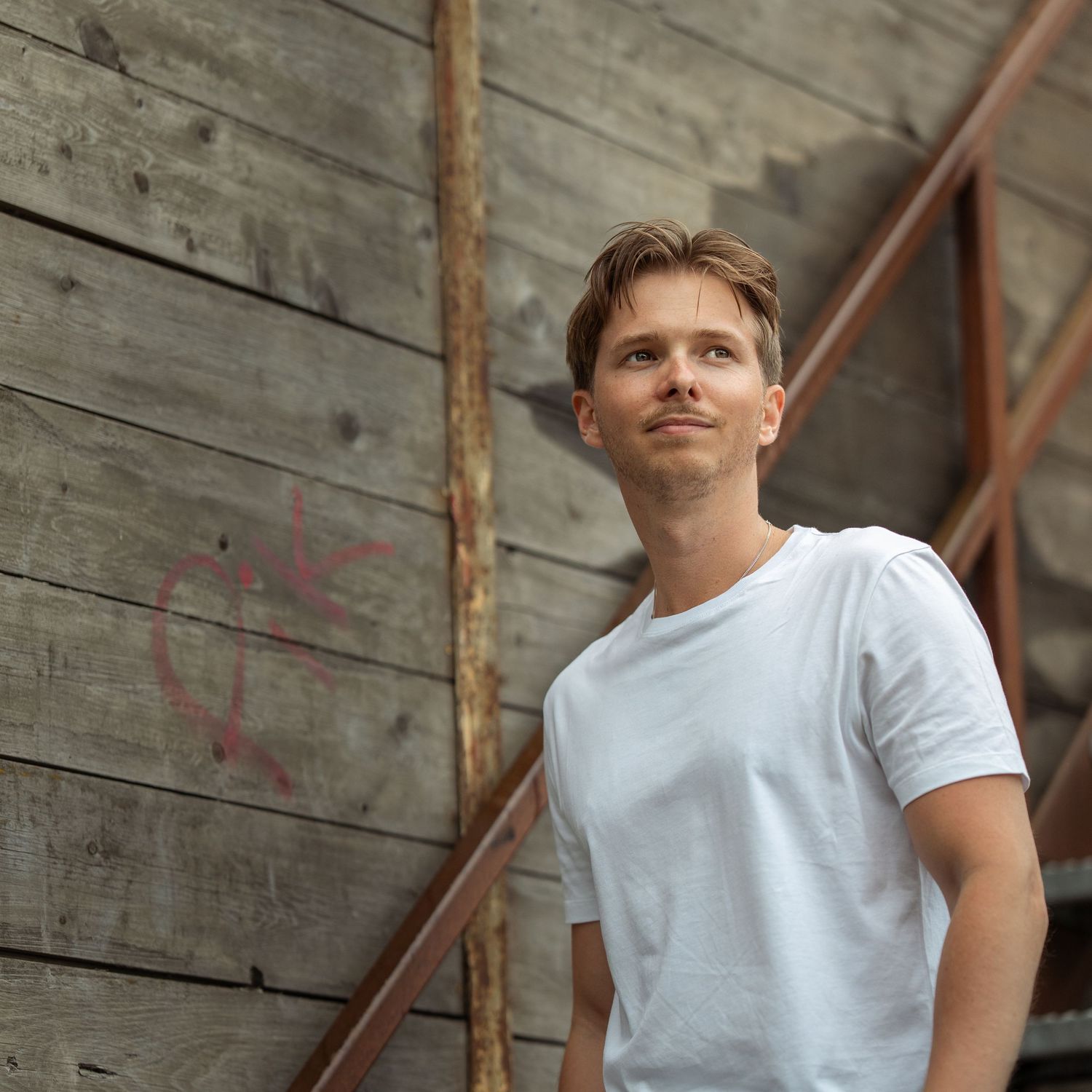 Young athlete in white t-shirt and shorts poses against rustic wooden wall during outdoor photo session.