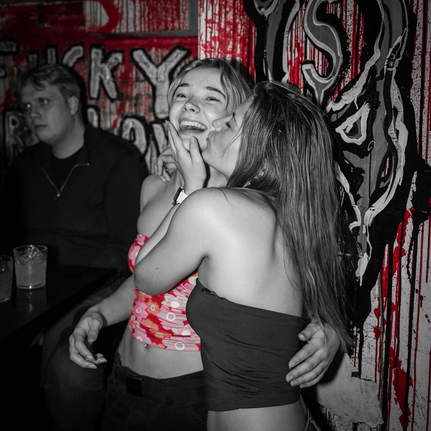 People dancing at a nightclub with red and black graffiti walls in a selective color photo.