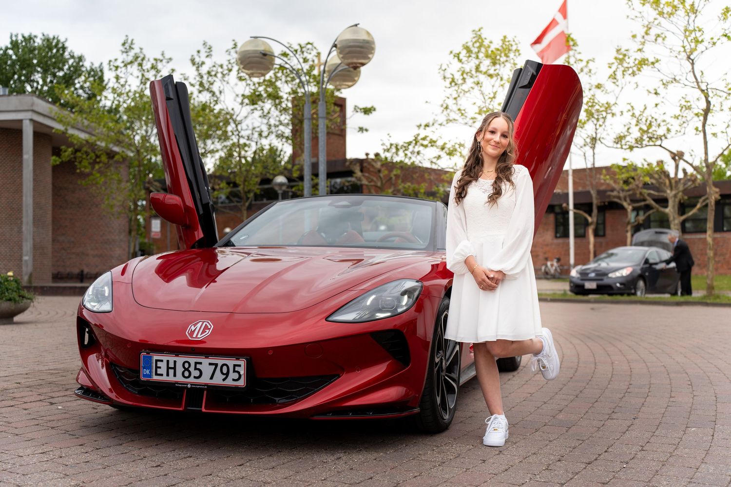 A red Tesla sports car with butterfly doors open stands parked in a circular driveway.