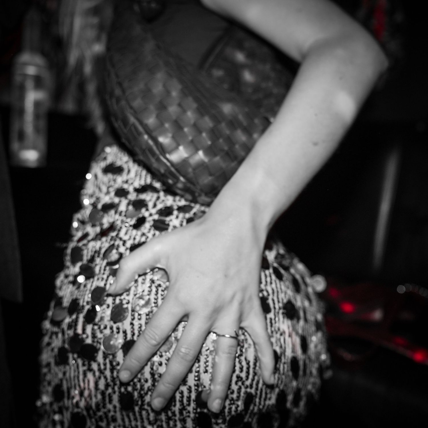 A black and white image shows a hand resting on a patterned dress or skirt in a dark nightclub setting.