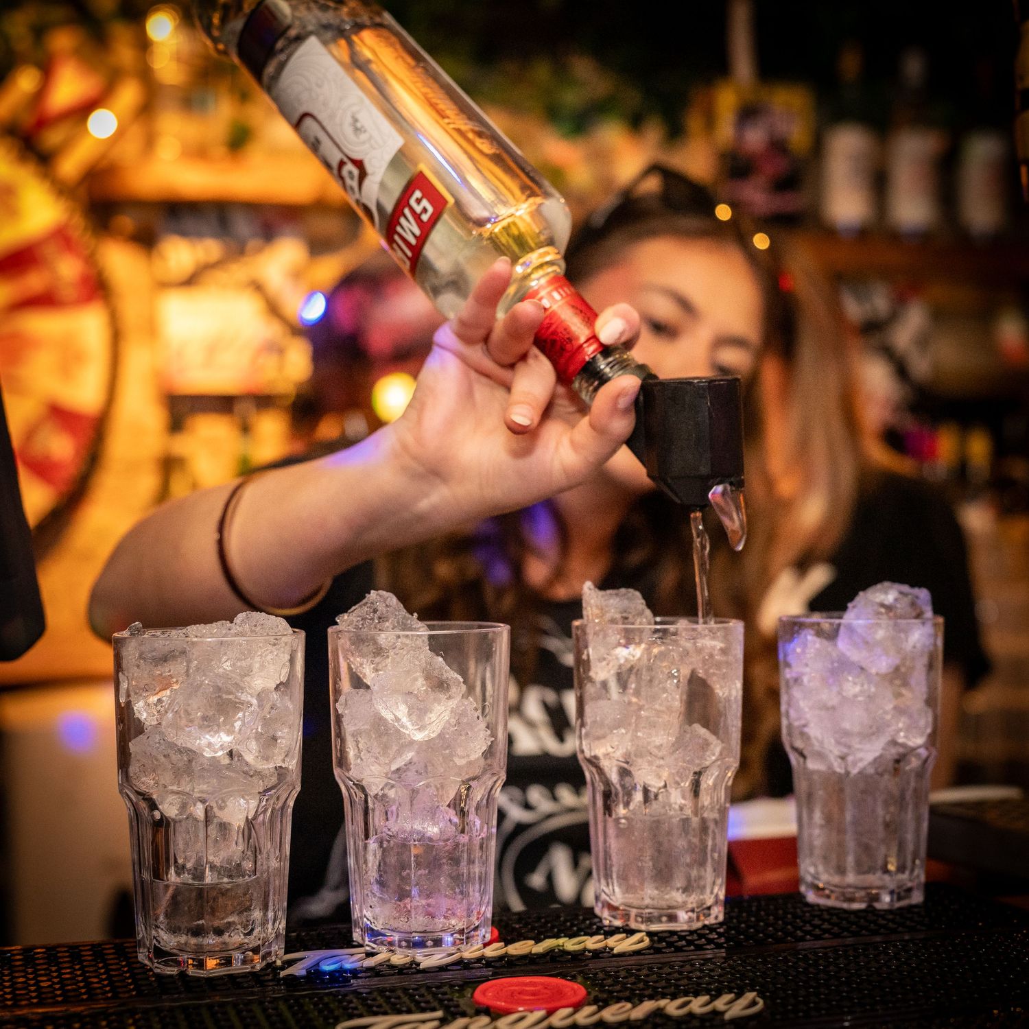 Bartender hælder spiritus i flere isfyldte glas på en bardisk.