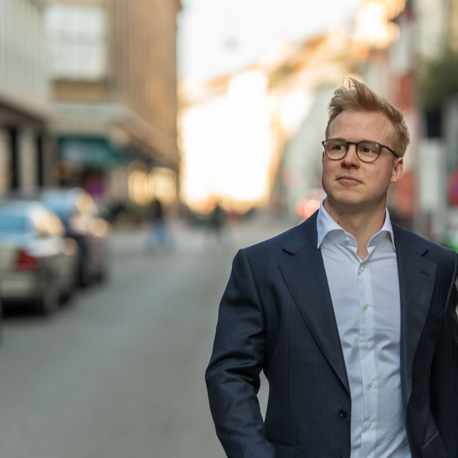 Person i mørkeblå jakkesæt går i indre by København ved solnedgangen.