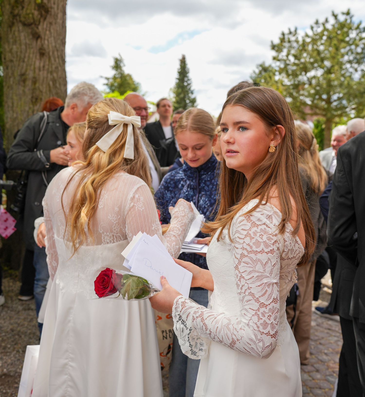 Wedding attendees in white lace dresses gather outdoors on a cloudy day during a celebration ceremony.