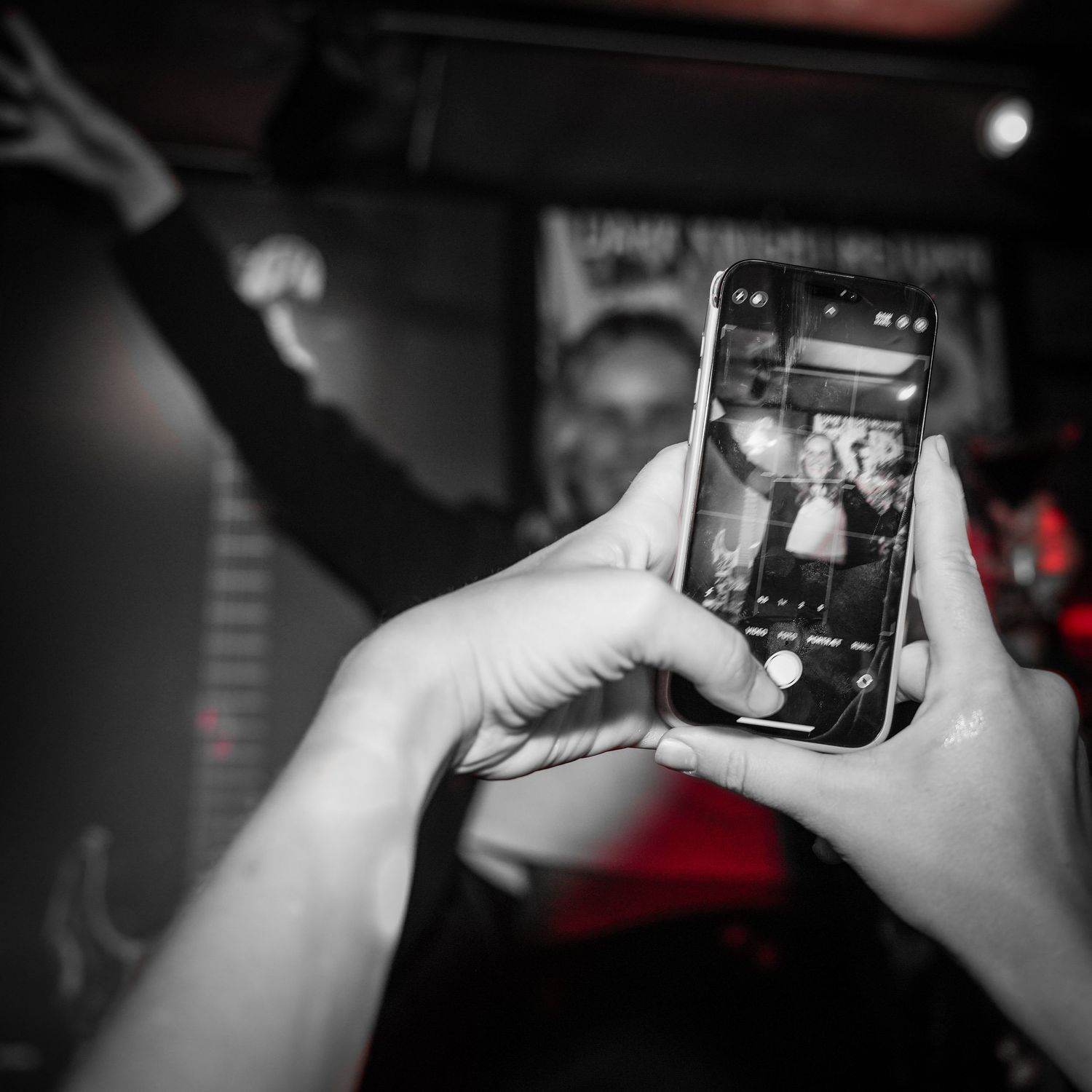 Someone uses a smartphone to take a photo at a concert or event in a dark venue with selective color on the phone.