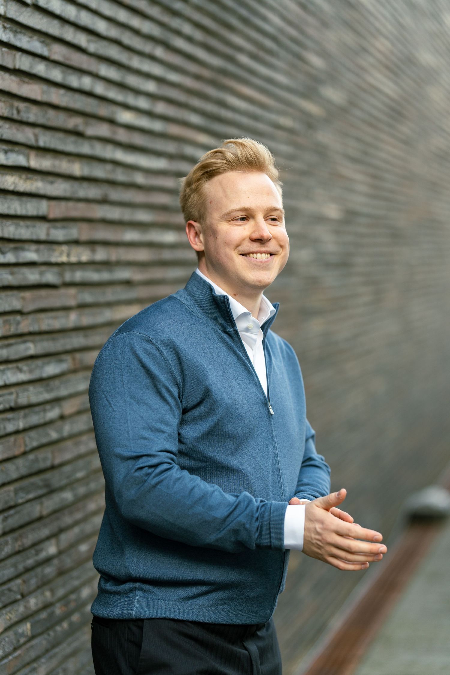 Casual business portrait in blue sweater against textured wall.