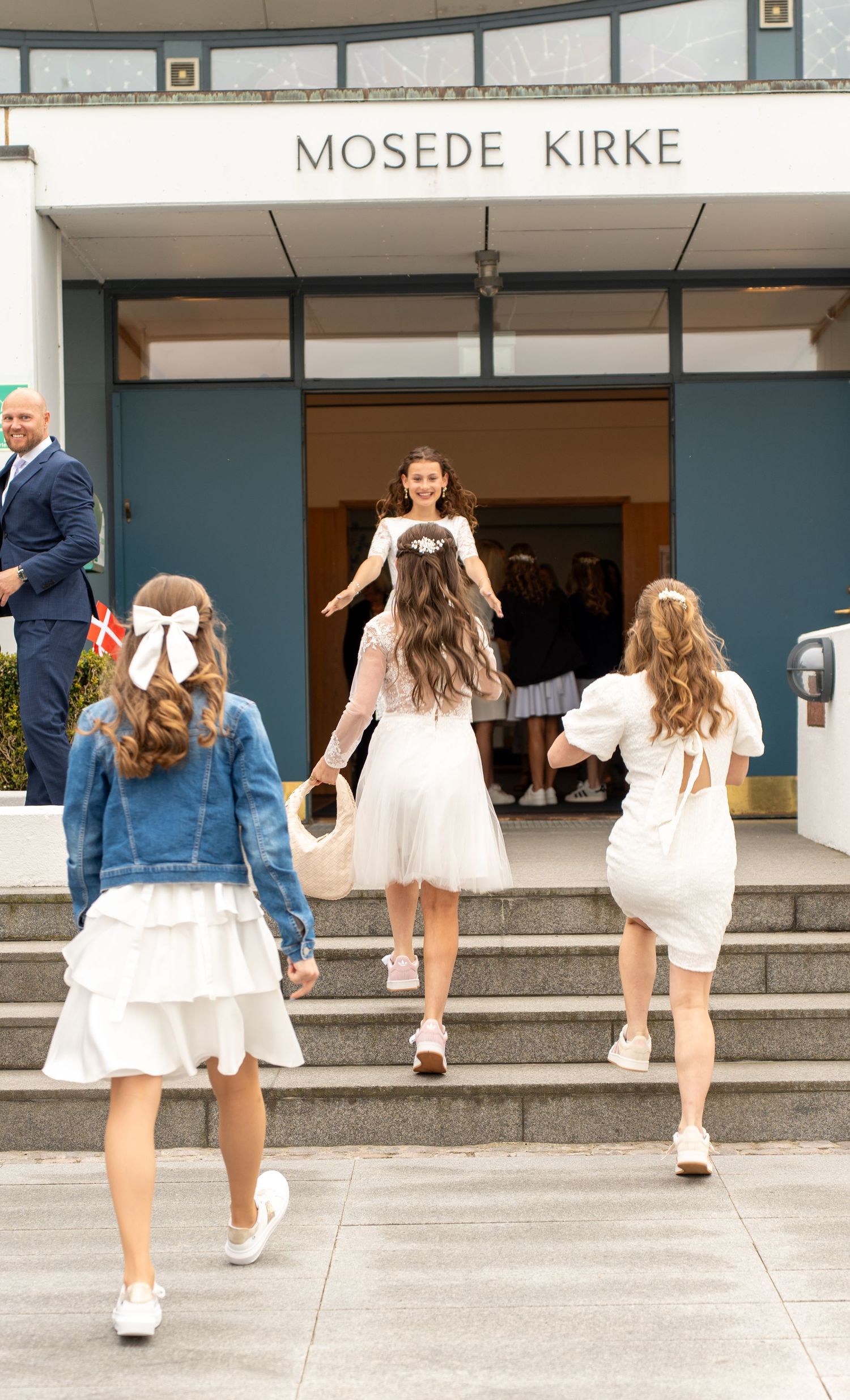 Young people in white dresses enter through the doors of Mosede Kirke church on stone steps.