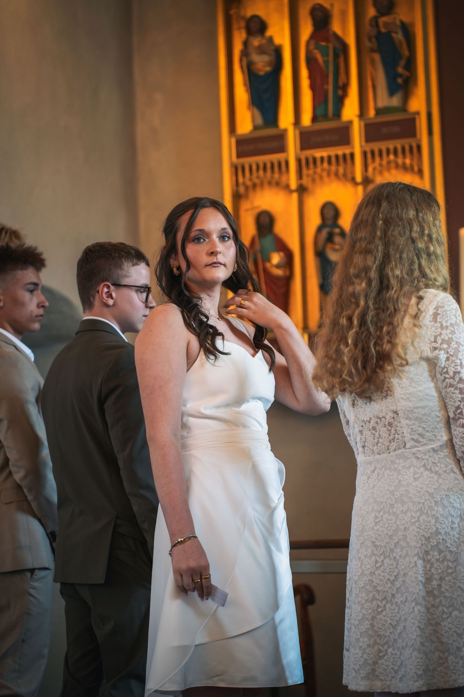 A wedding ceremony takes place in a church with ornate religious figures displayed in golden-lit alcoves behind the group.