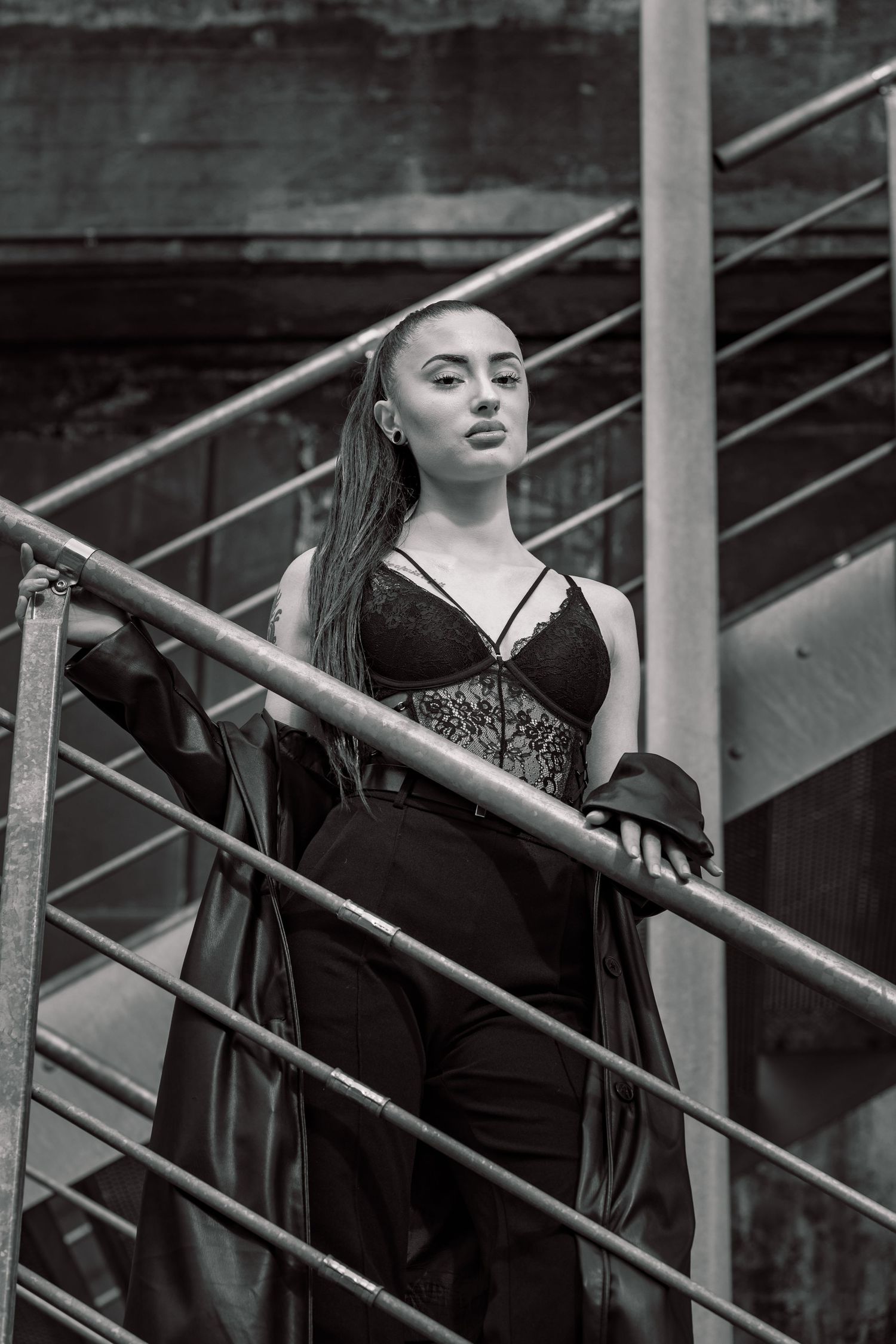 A black and white photo shows a figure in dark clothing leaning dramatically along a metal railing of ascending stairs.