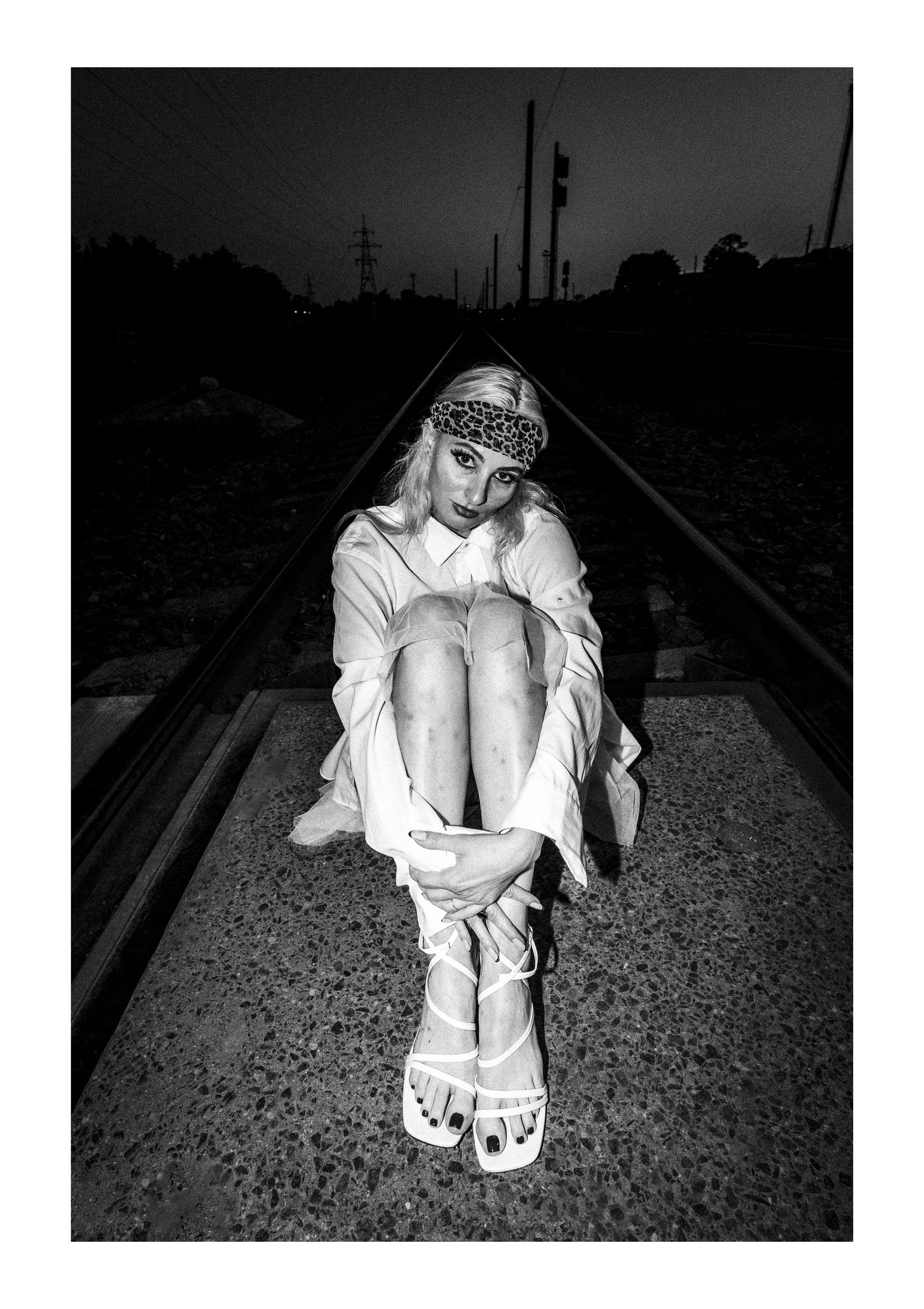 A black and white photo series shows a figure in white clothing sitting despondently along train tracks.