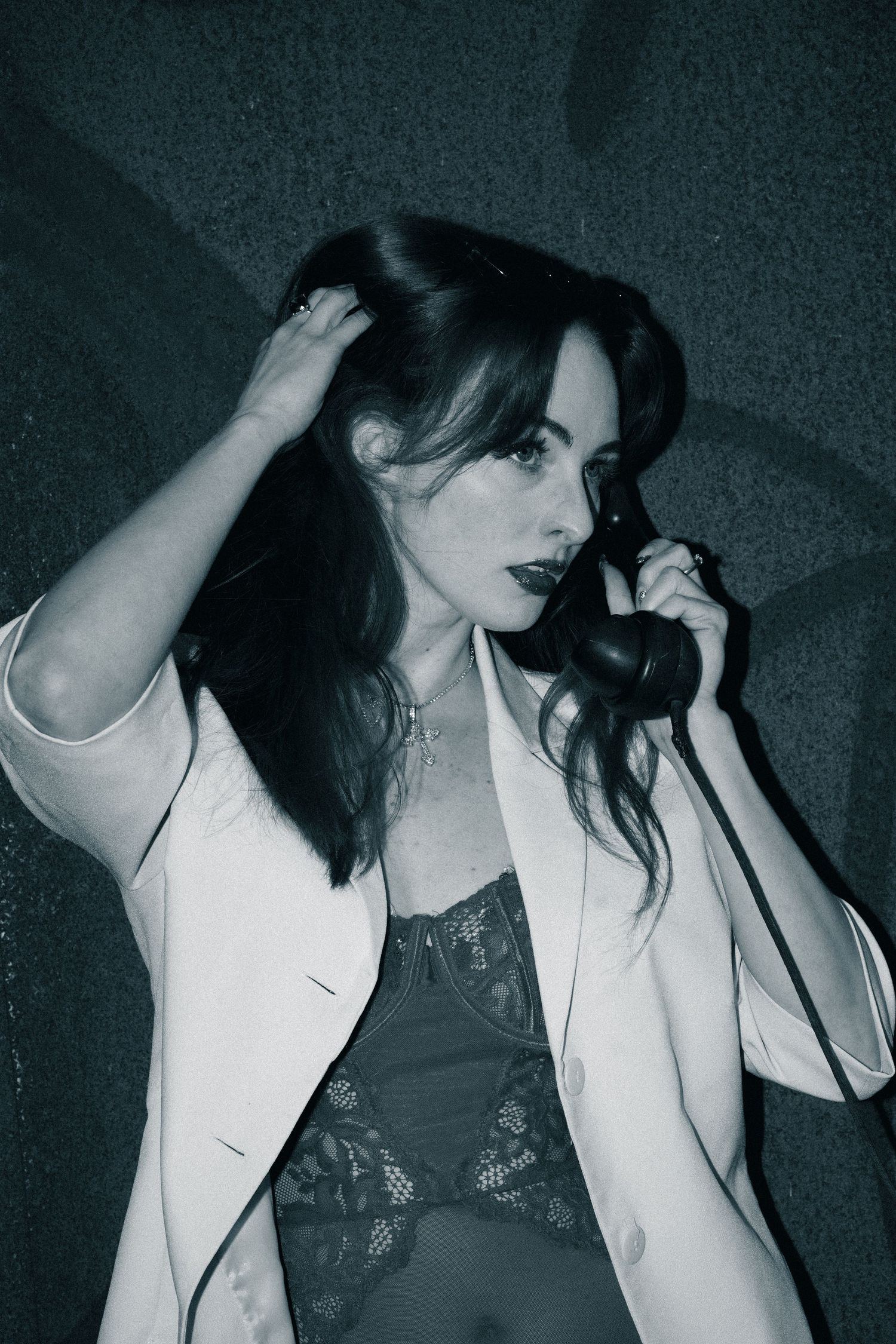 Black and white photo shows someone in lingerie and a white blazer talking on a vintage telephone.