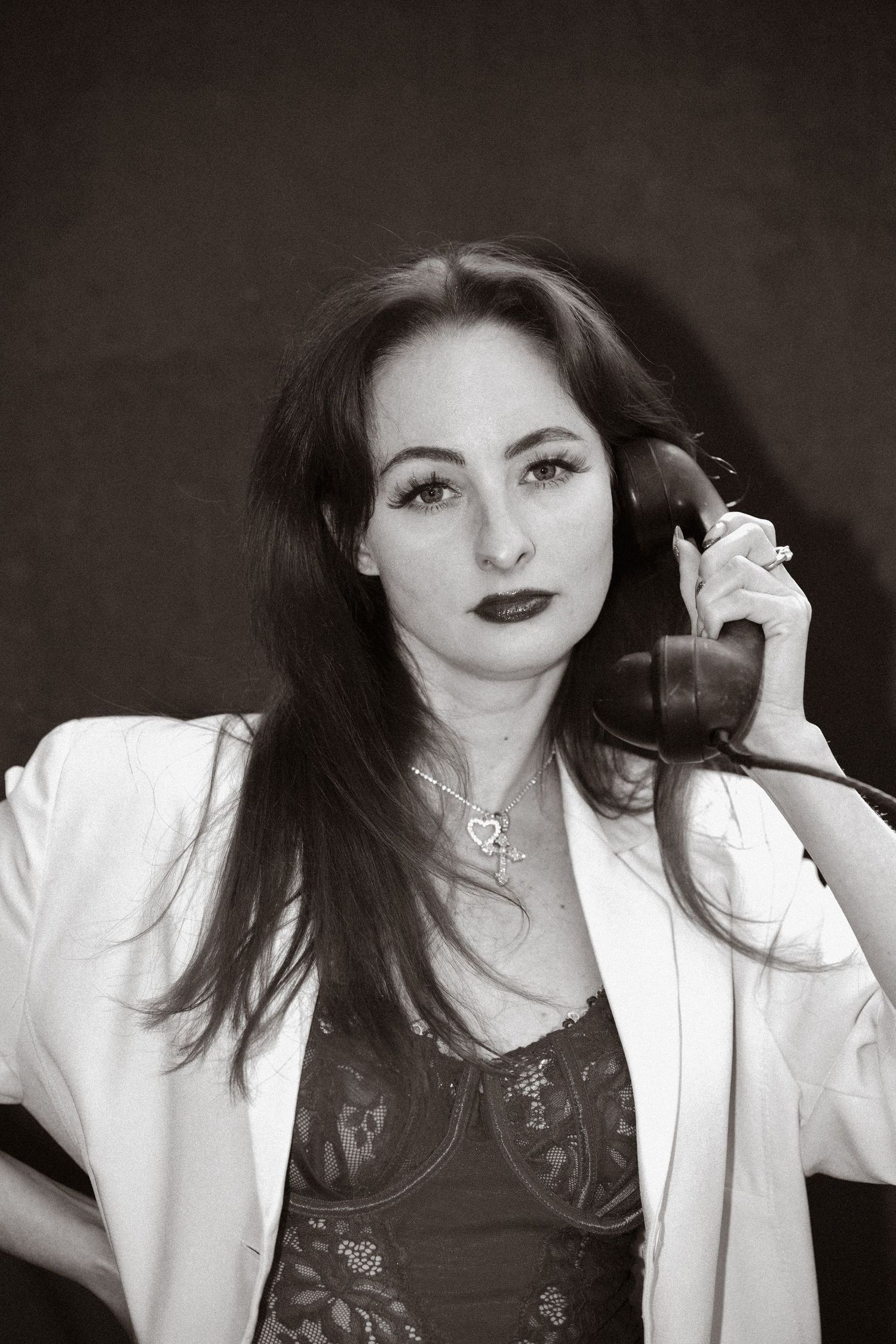A black and white portrait of someone in a white blazer holding a phone, with dark lipstick and long dark hair.