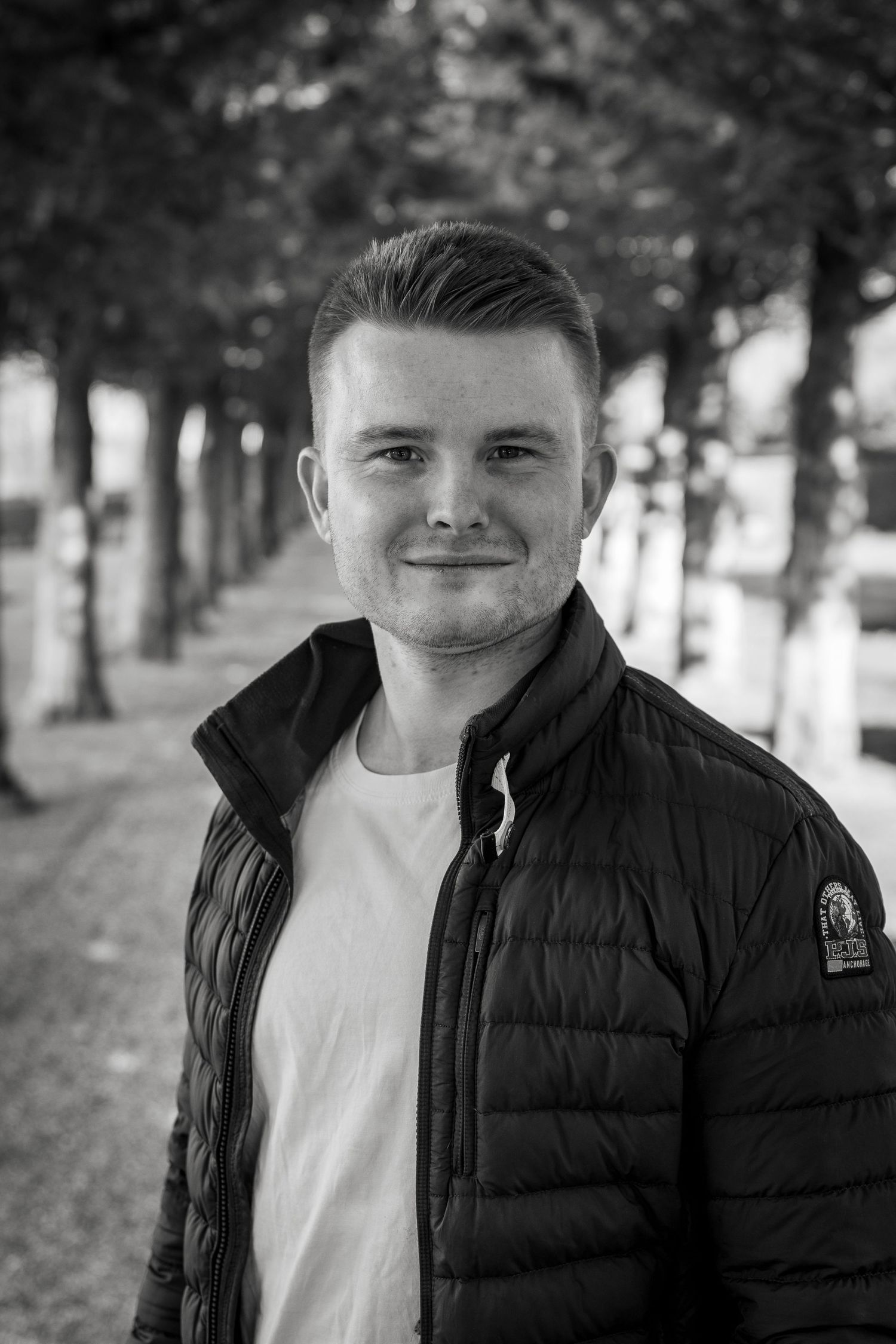 Sort hvidt portræt i efterårsomgivelser med en allé af træer.