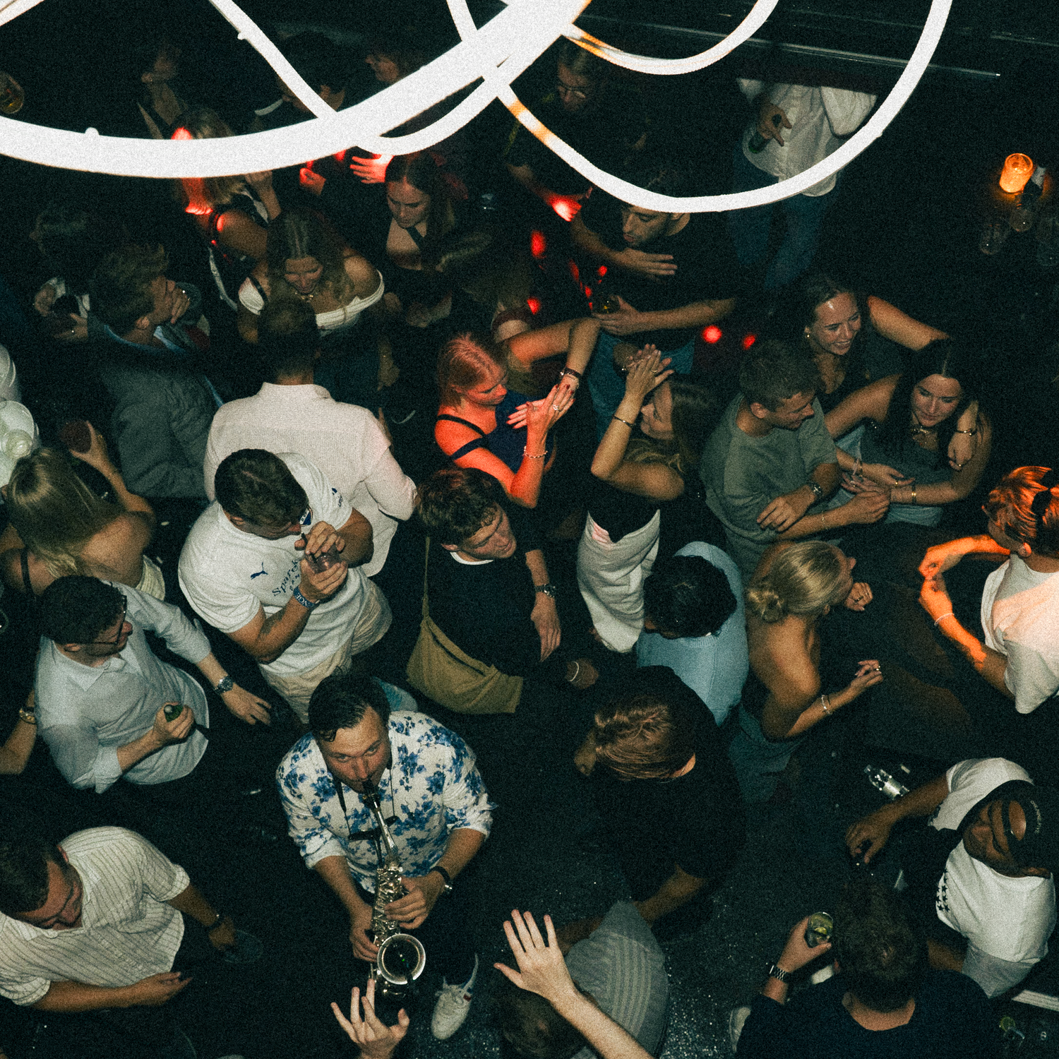 Crowded nightclub dance floor with colorful neon lights overhead showing people dancing and enjoying themselves at night.
