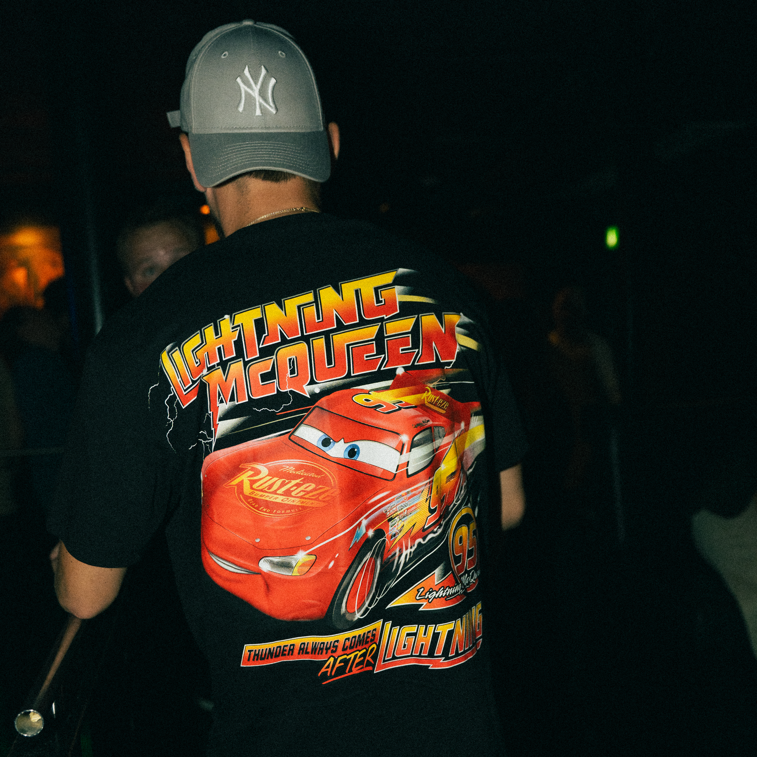 Close-up details of Lightning McQueen character merchandise including t-shirts and hats in a dark retail setting.