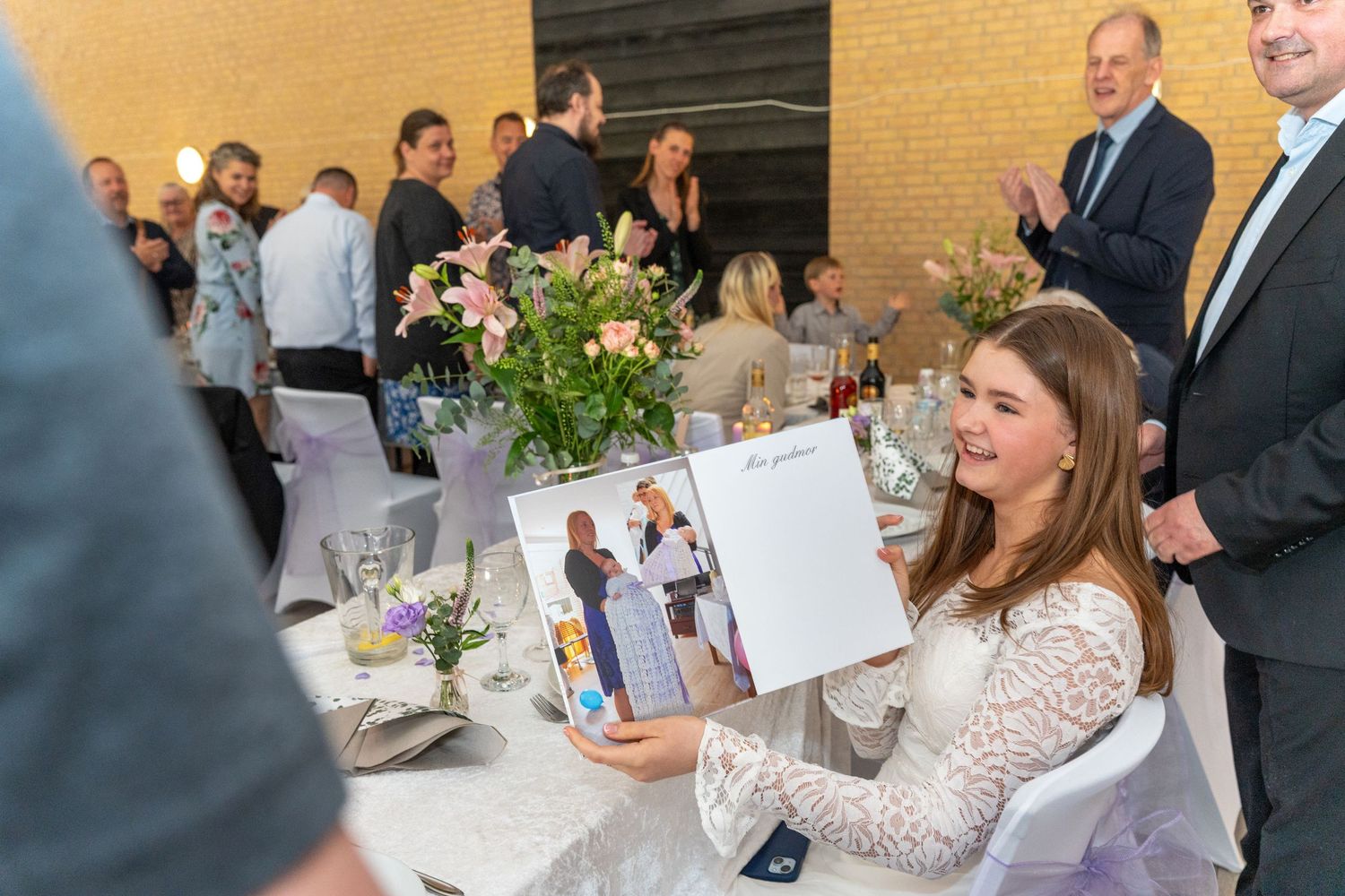 Attendees gather at an elegant reception with floral centerpieces and photo displays on decorated dining tables.